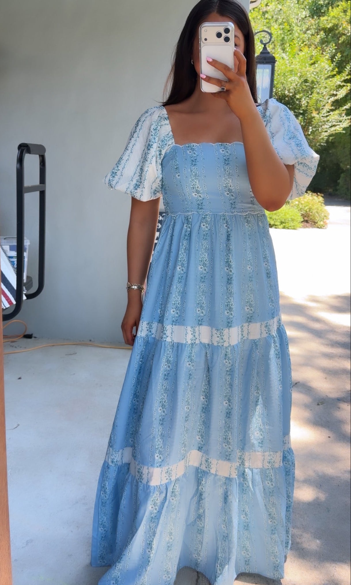 Woman wearing a blue lace dress taking a mirror selfie outdoors.