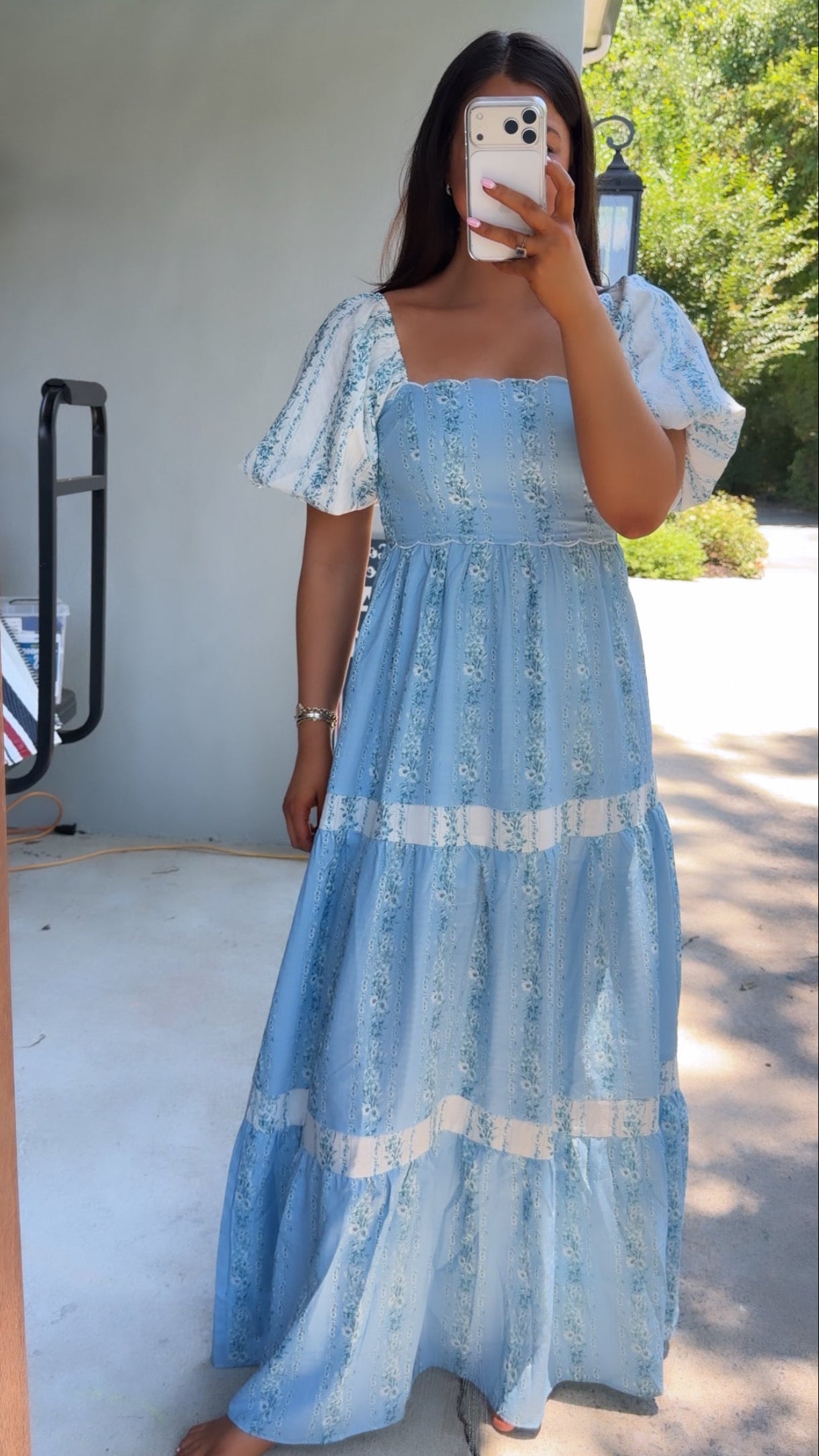 Woman wearing a blue lace dress taking a mirror selfie outdoors.