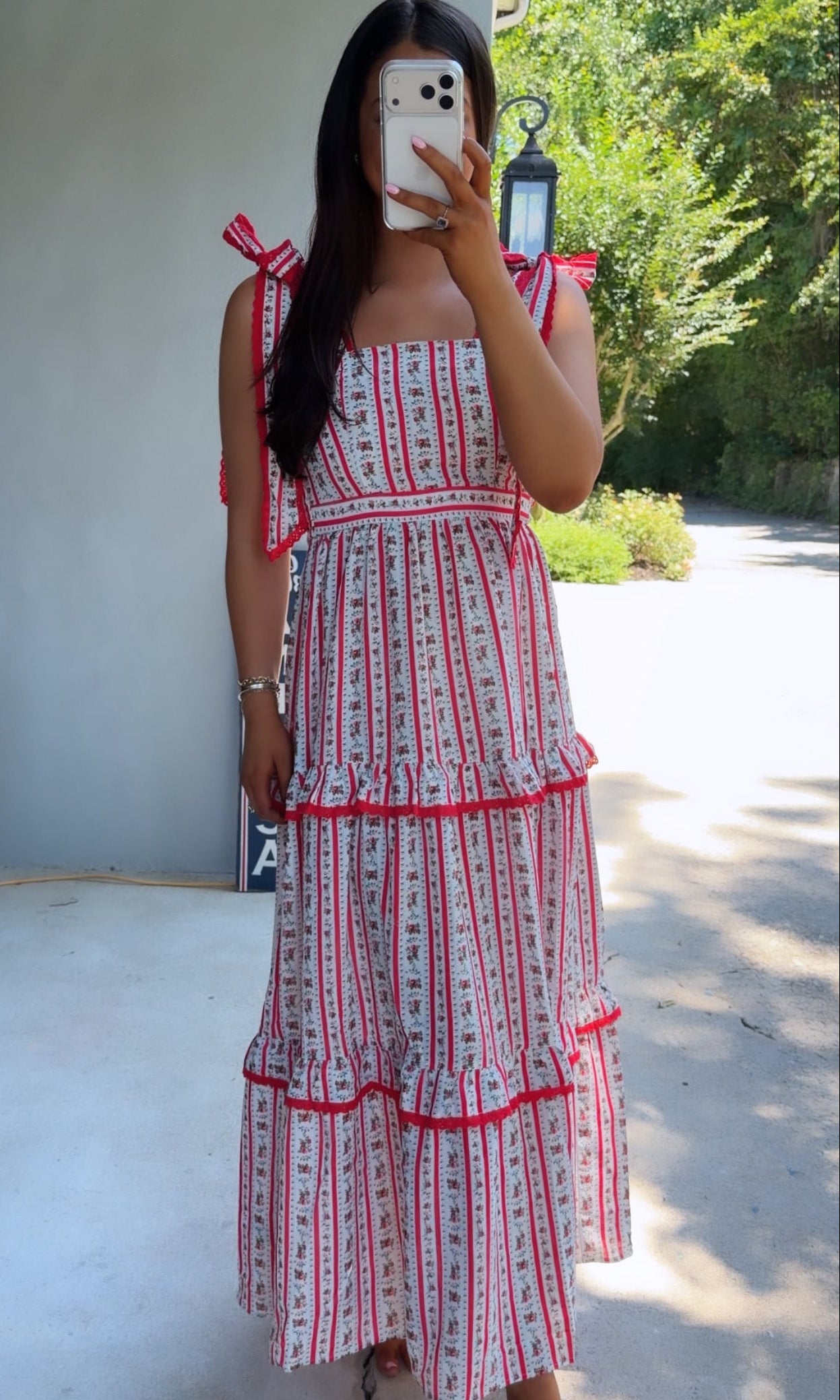 Woman wearing a red and white patterned dress taking a mirror selfie outdoors.