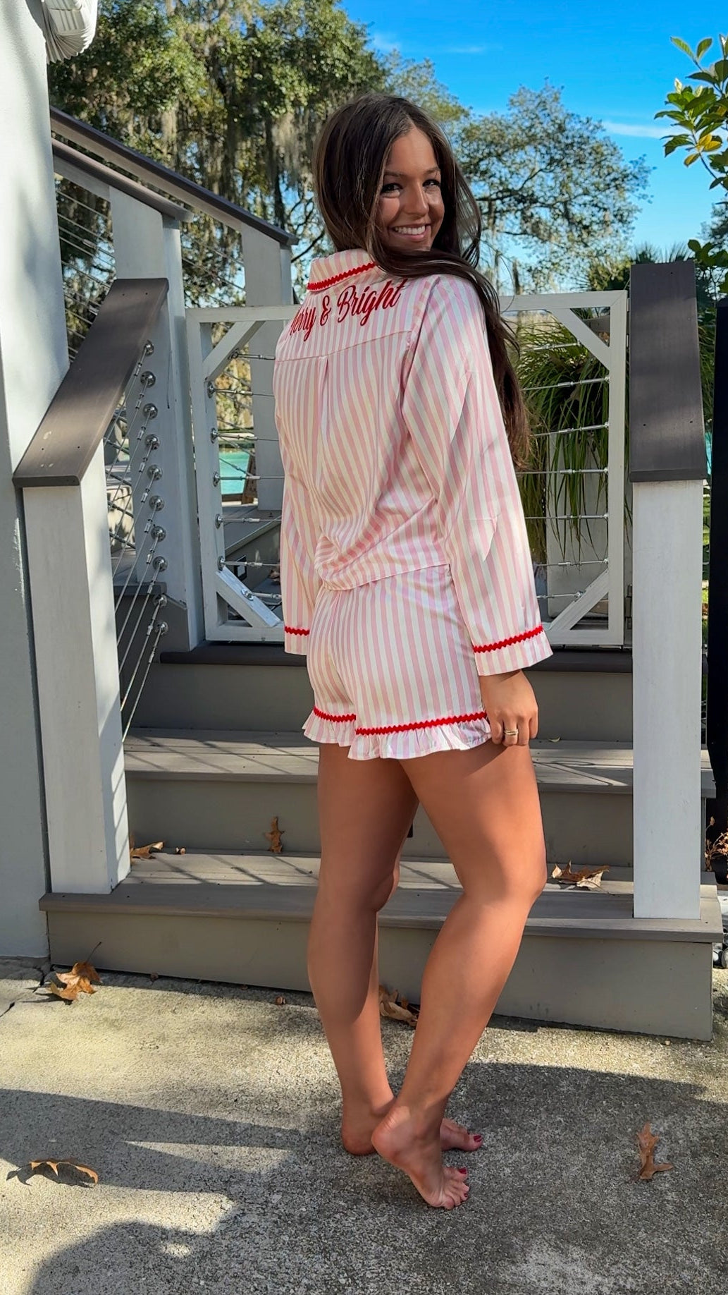 Woman wearing a pink and white striped pajama set with red accents outdoors. christmas pajamas merry and bright wording on back