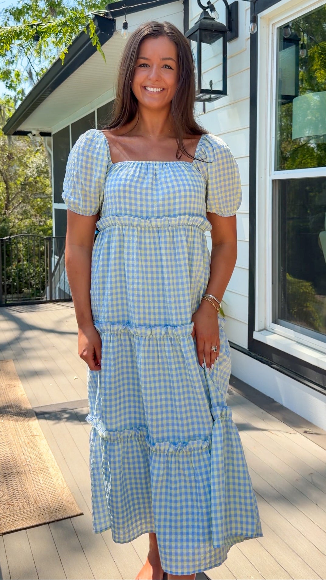 Woman wearing a blue and white checkered dress standing on a wooden deck.