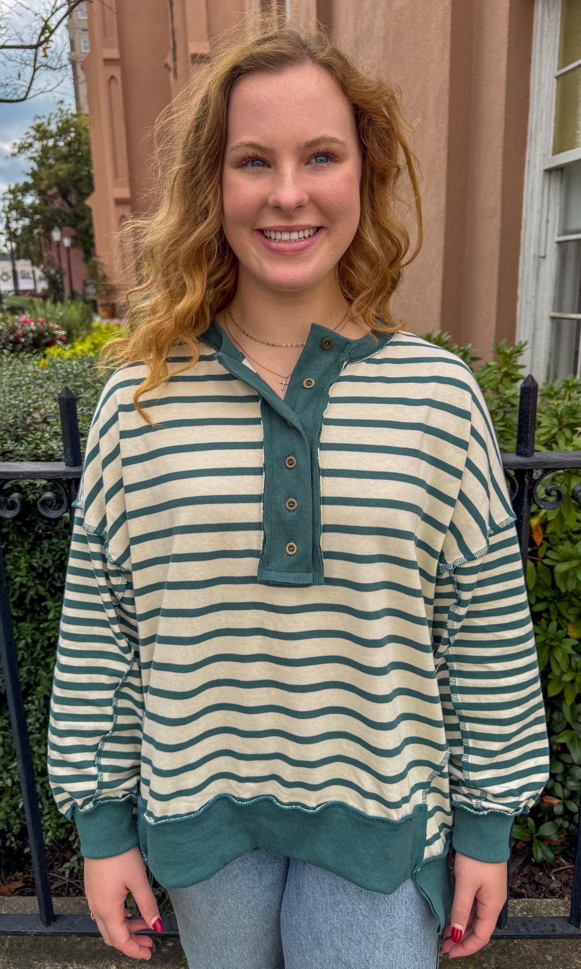 Woman wearing a striped shirt with green accents standing outdoors.