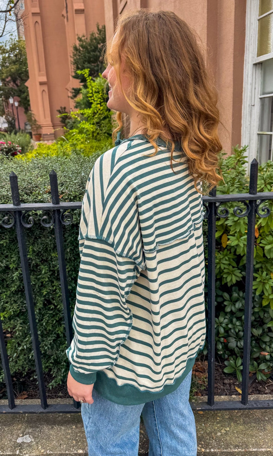 Woman wearing a green and white striped sweater and blue jeans standing outdoors.