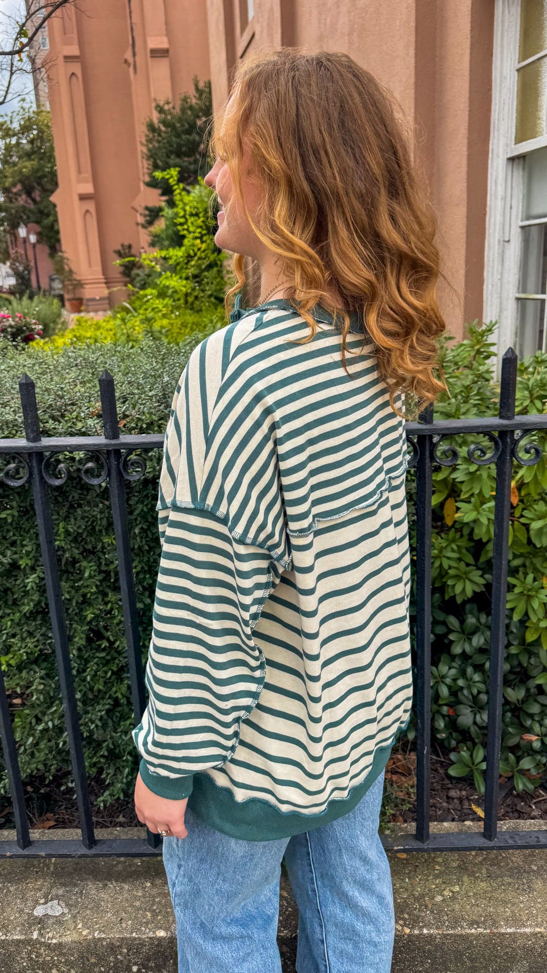 Woman wearing a green and white striped sweater and blue jeans standing outdoors.