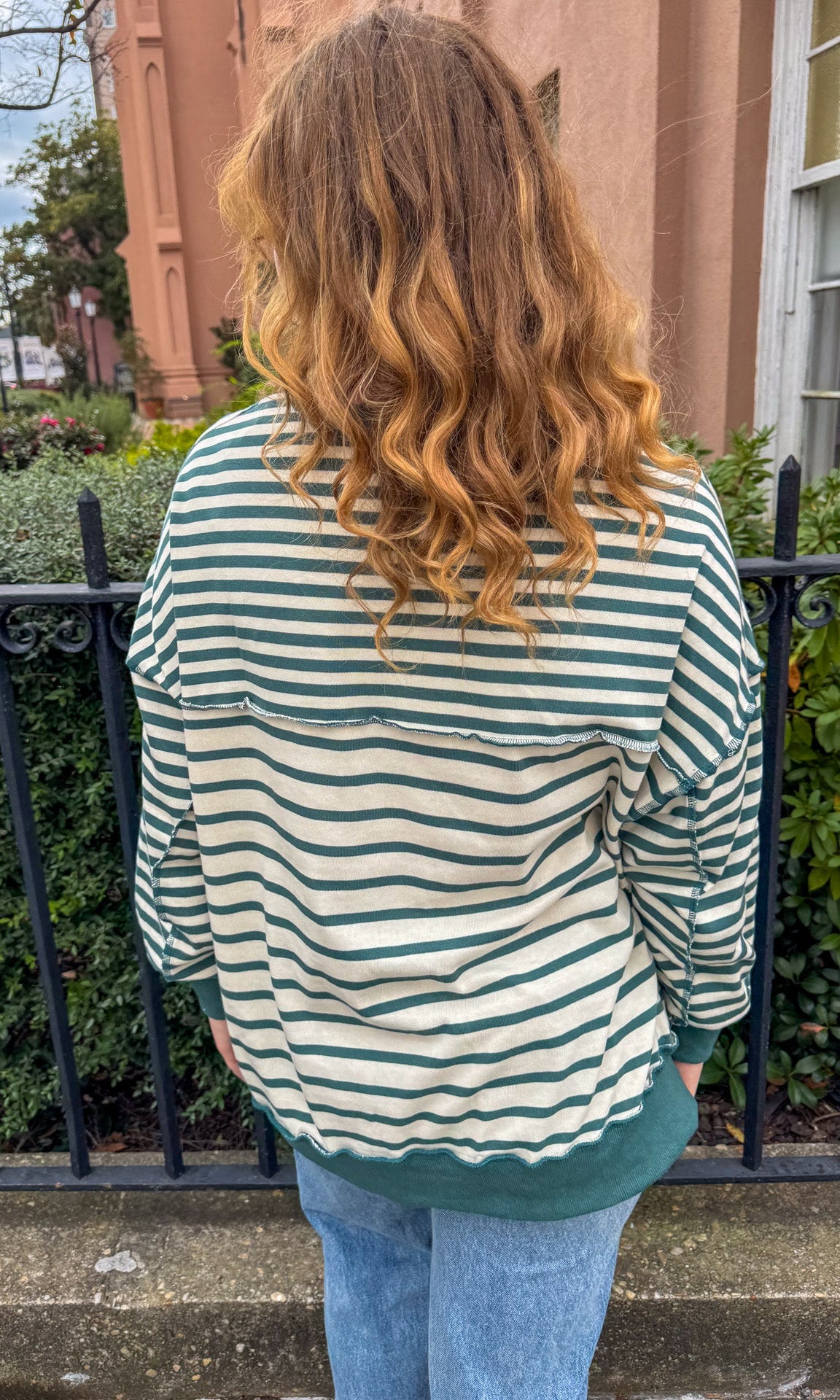 Person wearing a green and white striped shirt standing outdoors with a building and trees in the background.