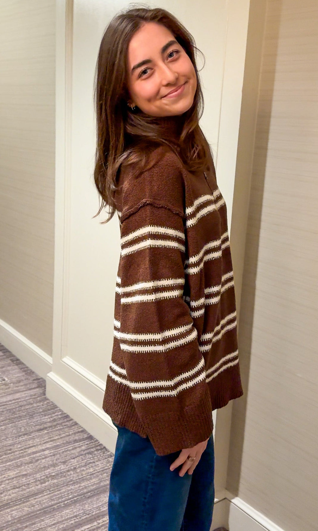 Woman wearing a brown and white striped sweater in a hallway.