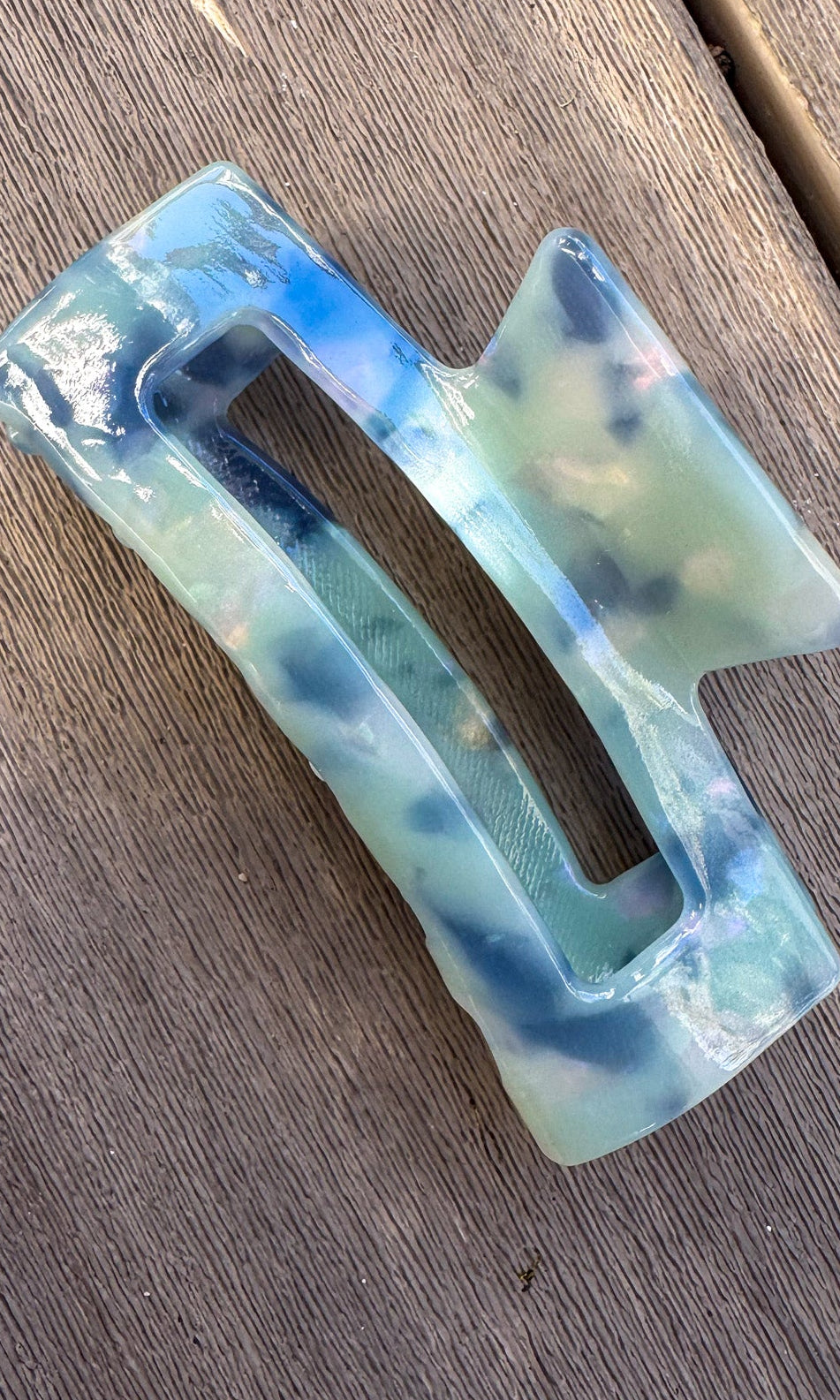 Decorative hair clip with blue and green gradient on a wooden surface