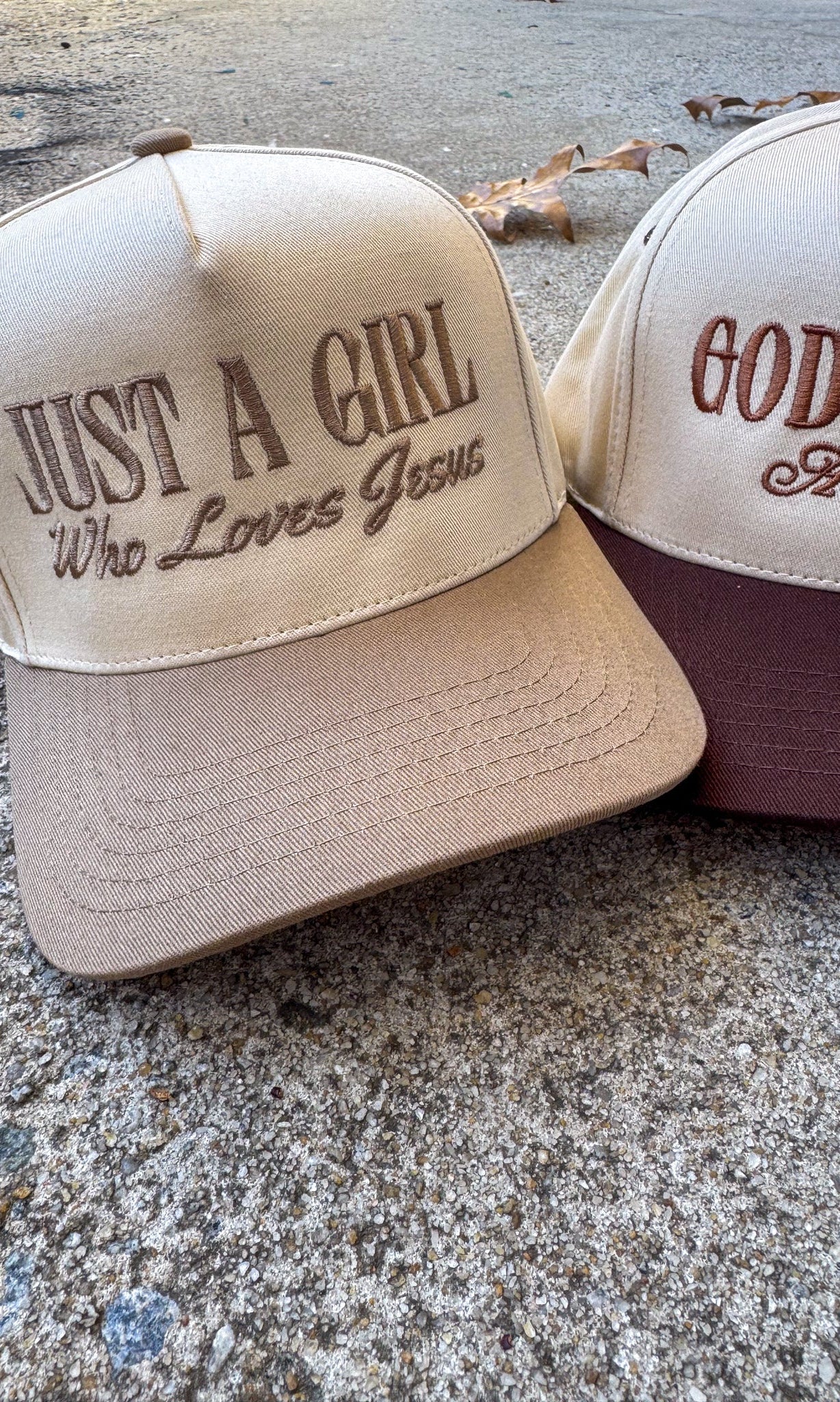 Two baseball caps with embroidered text on a concrete surface