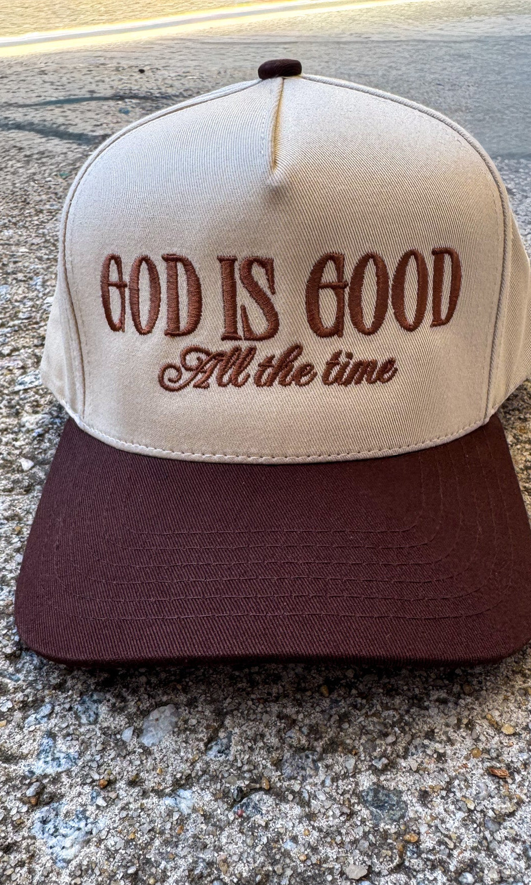 Cap with 'God is Good All the time' text on a concrete surface, trucker hat, christian trucker hat brown