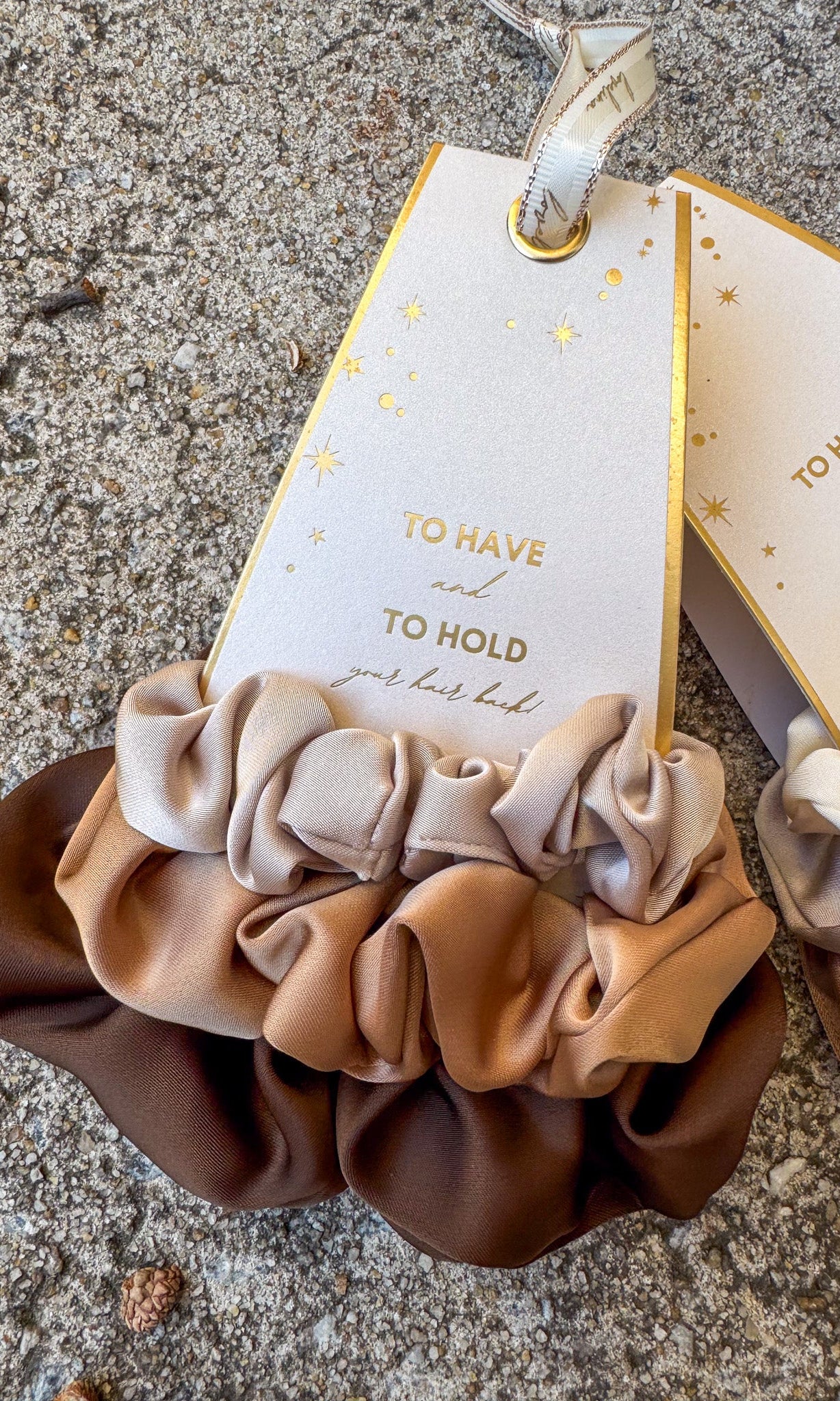 Set of three brown scrunchies with a decorative tag on a textured surface