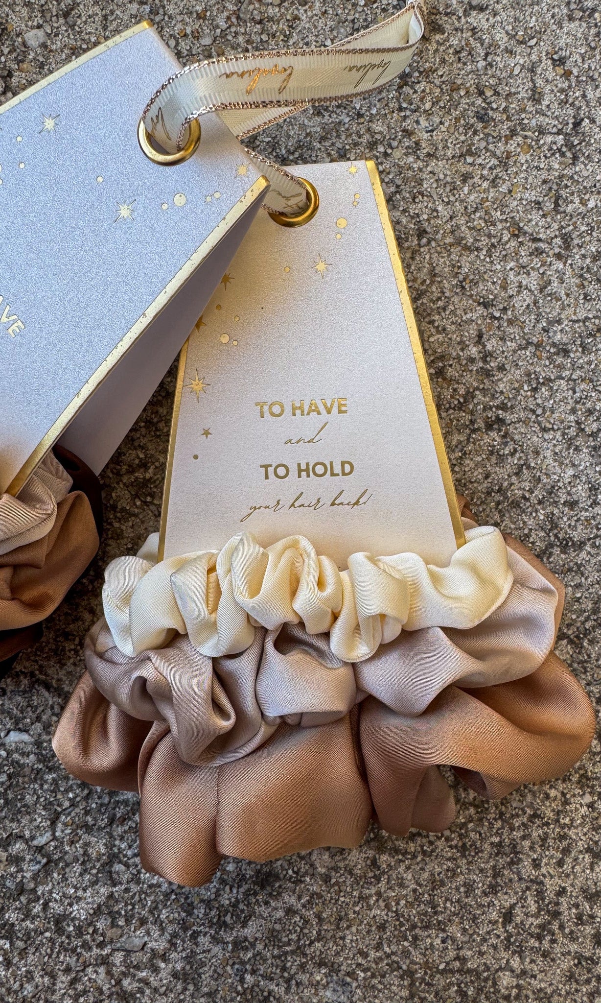 Set of beige scrunchies with a decorative tag on a textured surface