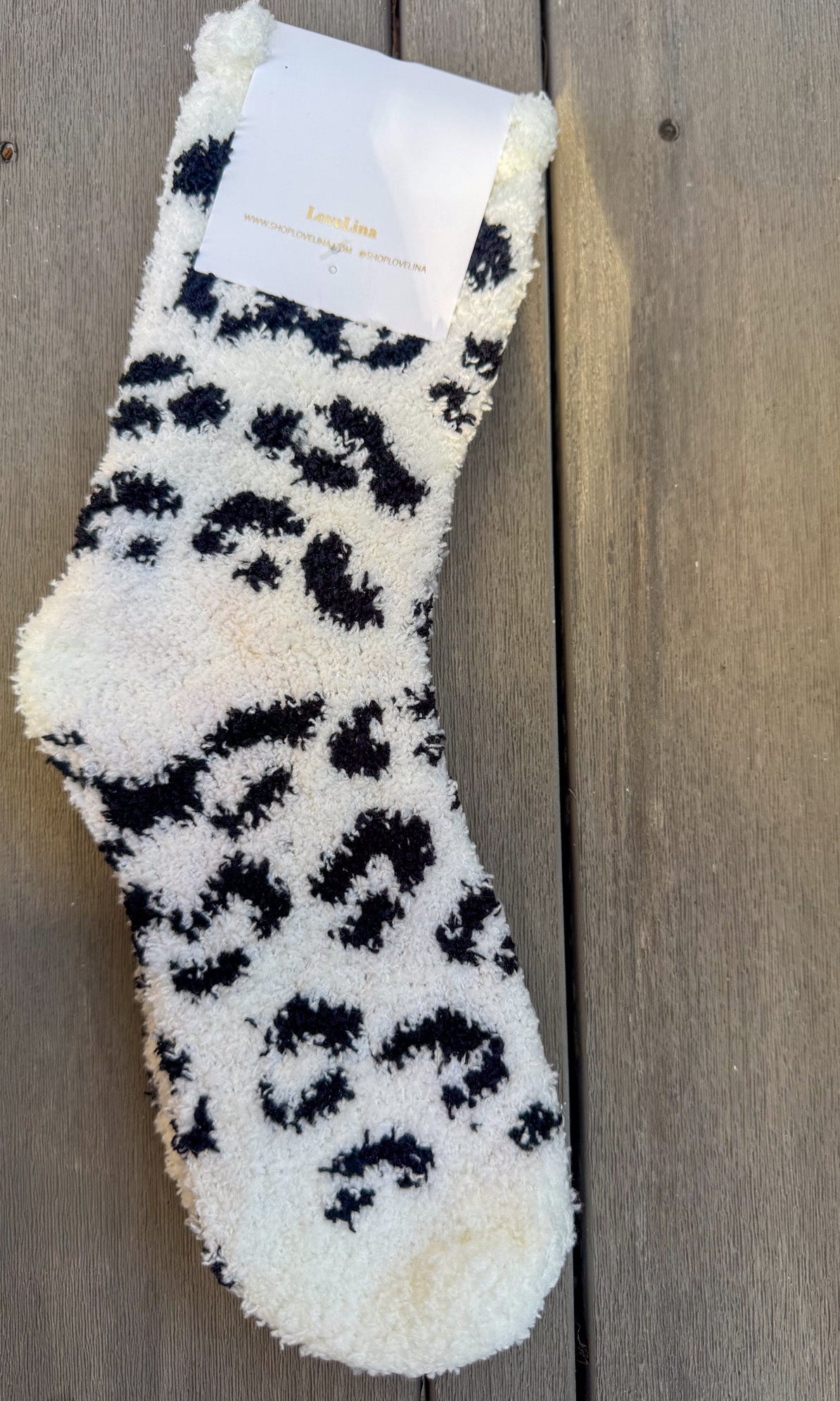 White fuzzy sock with black leopard print pattern on a wooden surface