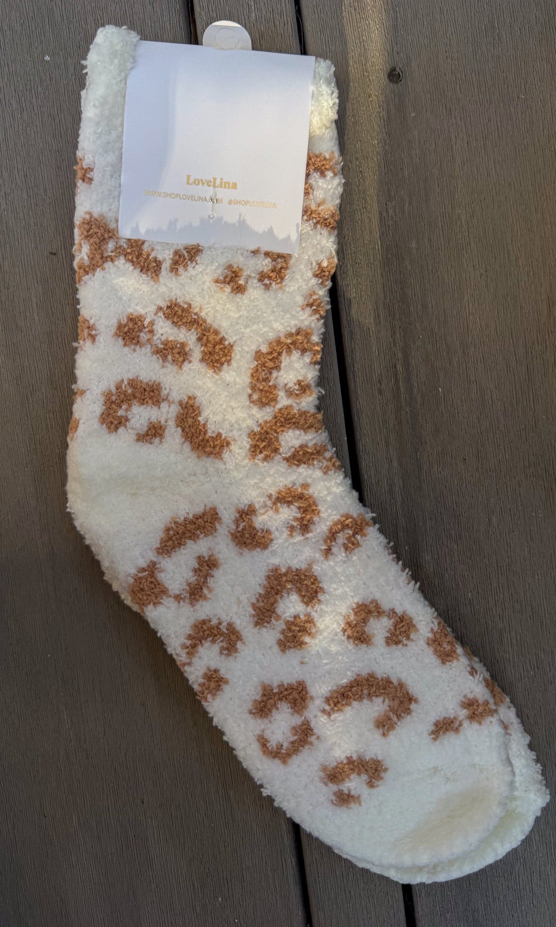 Fluffy white sock with brown leopard print pattern on a wooden surface