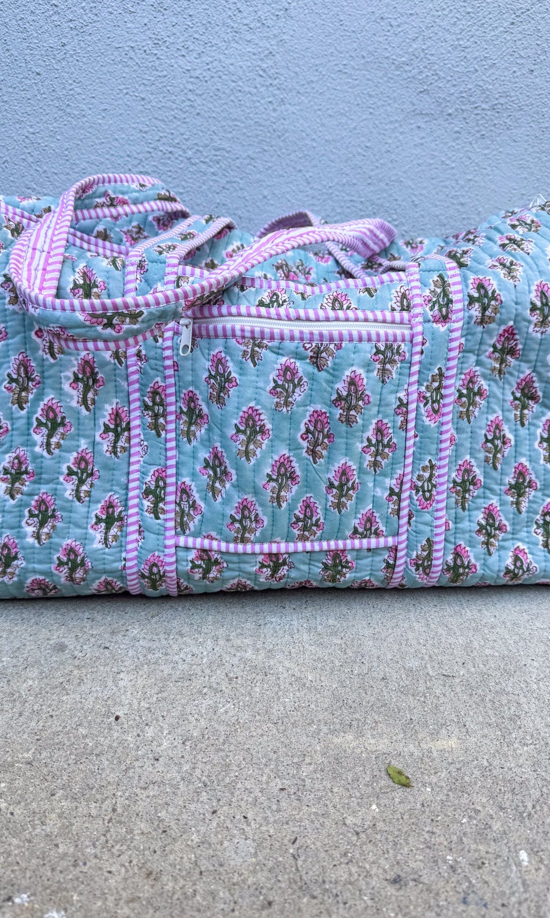 Floral patterned duffel bag with pink trim on a concrete surface.