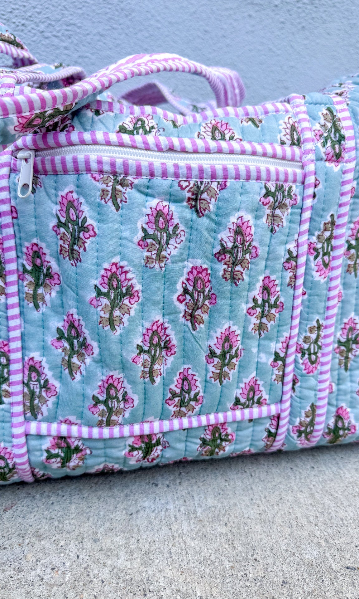 Floral quilt with pink and white striped trim on a concrete surface