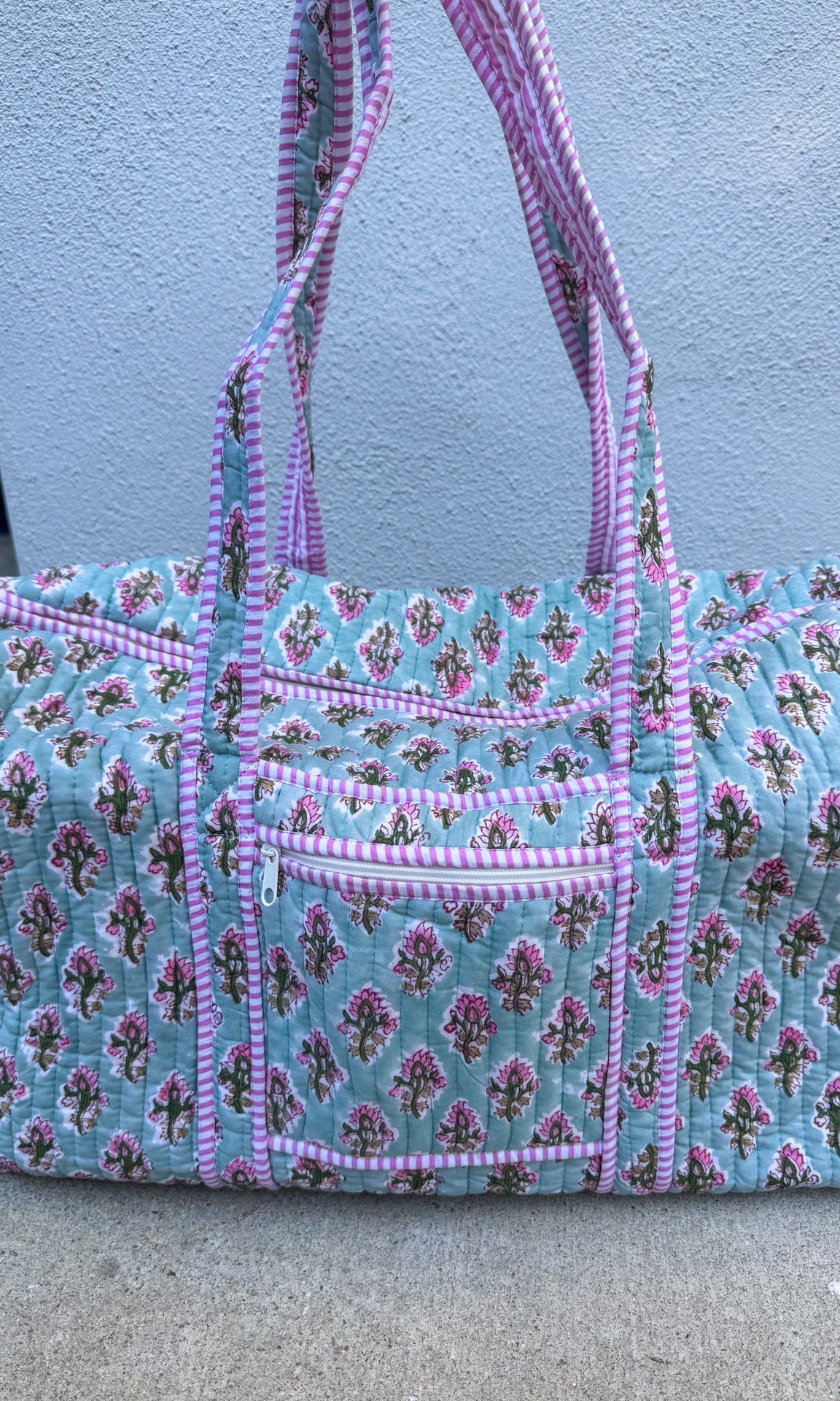 Floral patterned handbag with pink accents on a concrete surface.