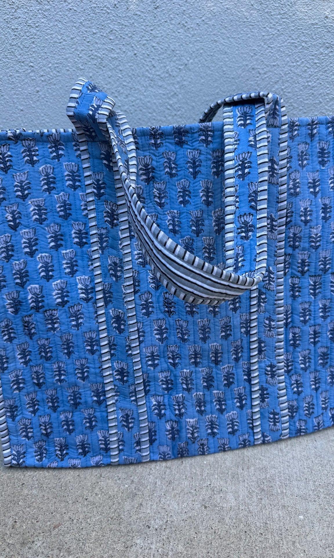 Blue textured tote bag with black handle on a gray surface