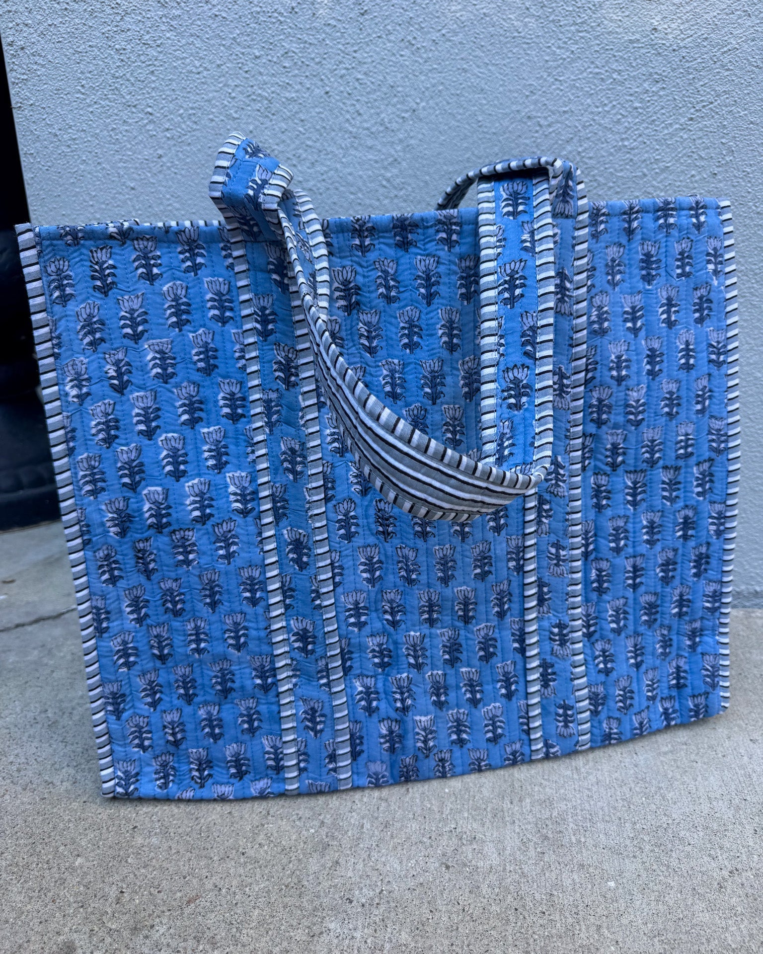 Blue textured tote bag with black handle on a gray surface