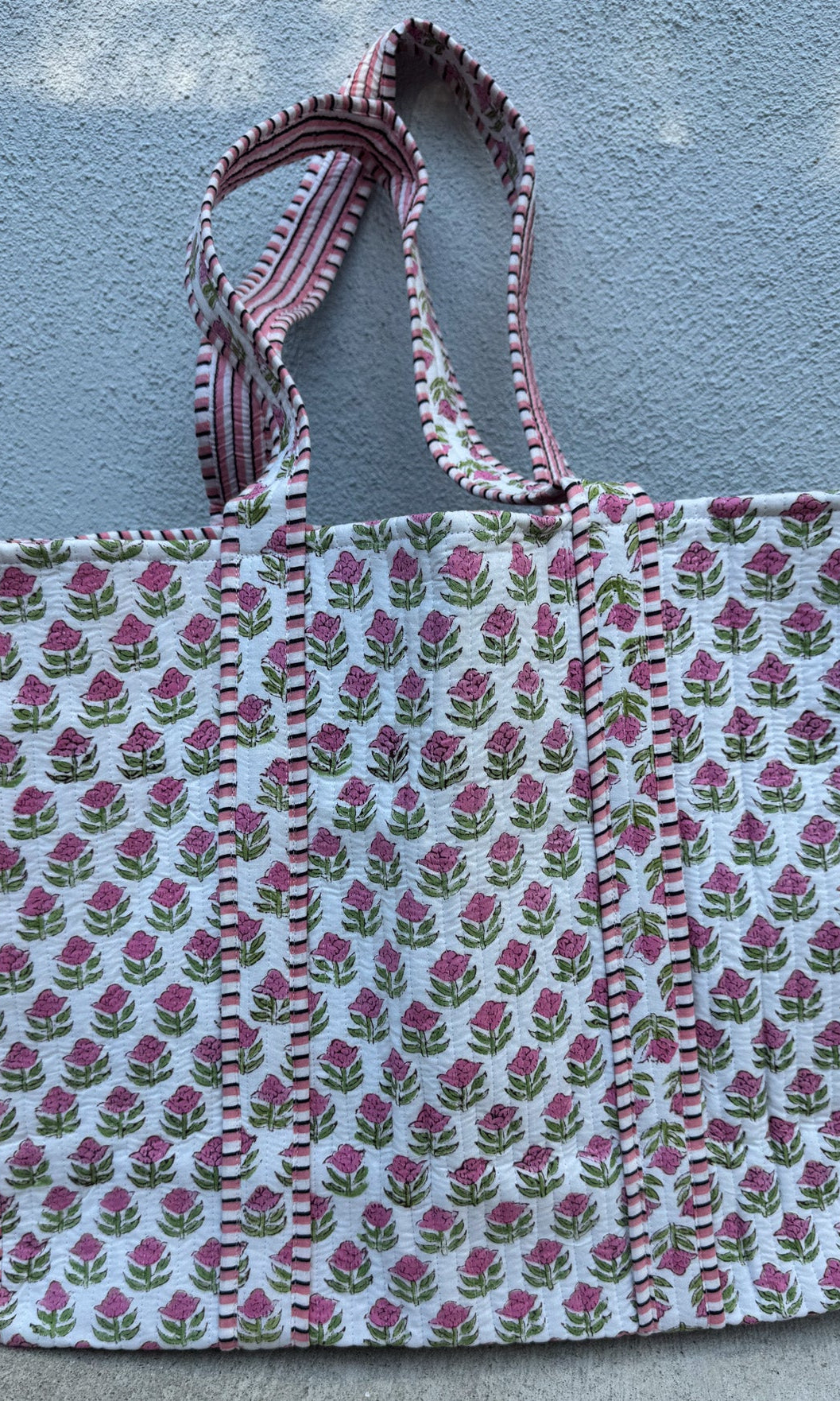 Floral patterned tote bag with striped handle against a textured wall.