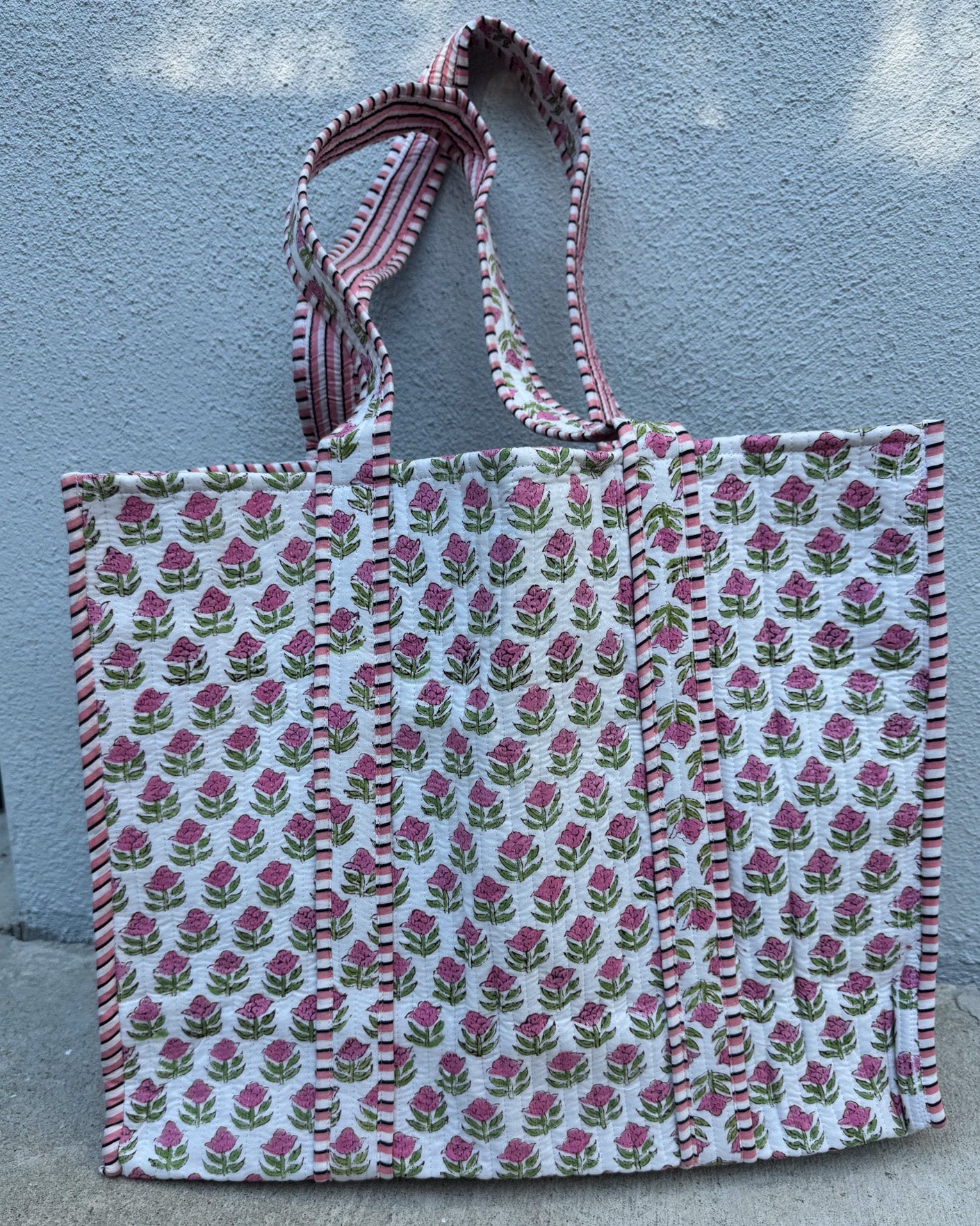 Floral patterned tote bag with striped handle against a textured wall.