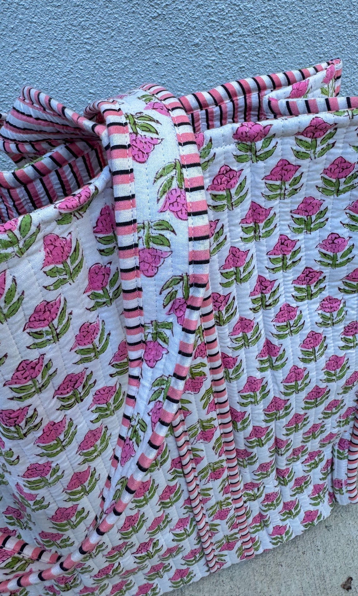 Floral-patterned fabric with pink flowers and green leaves on a white background, folded and leaning against a blue wall.