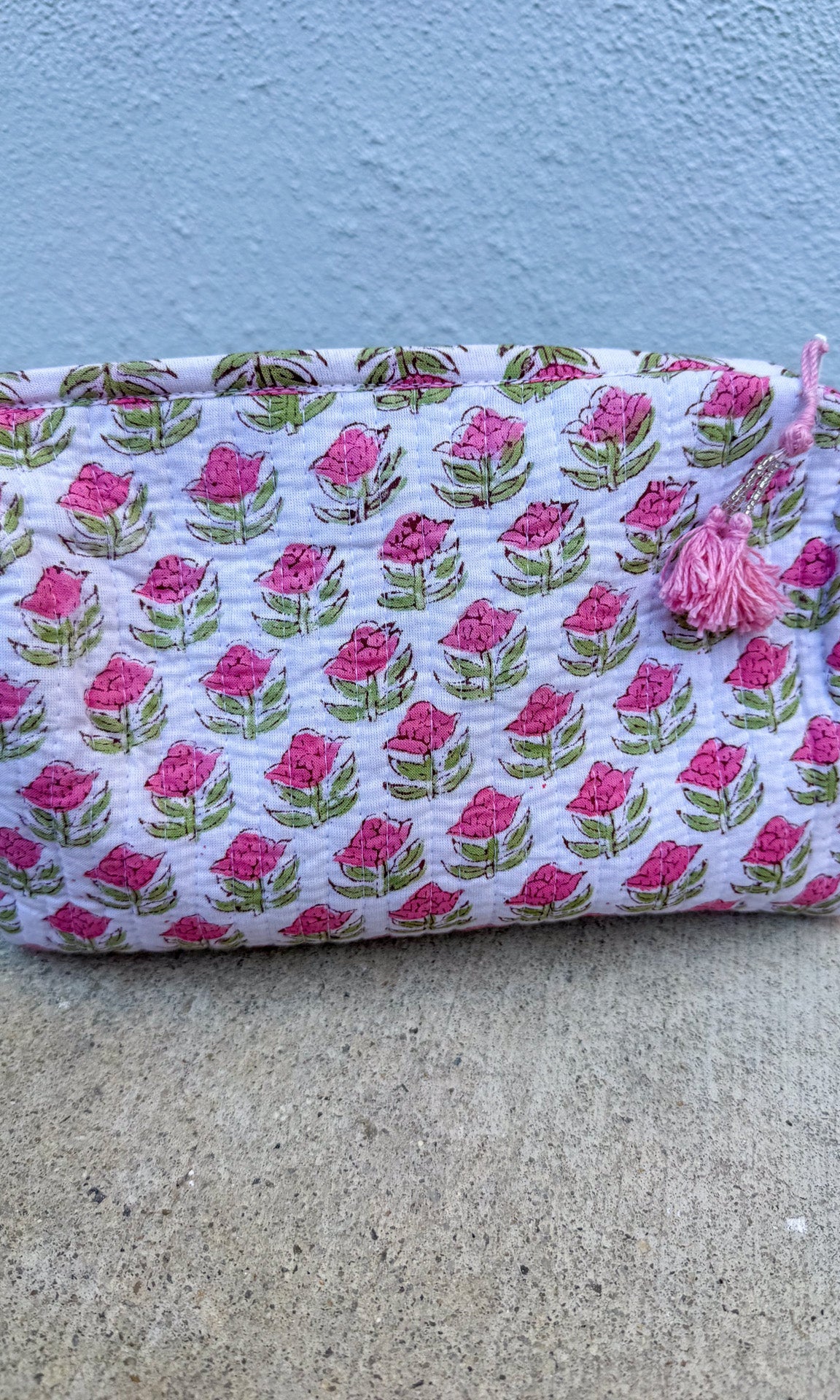 Fabric pouch with pink floral pattern on a concrete surface and blue wall background