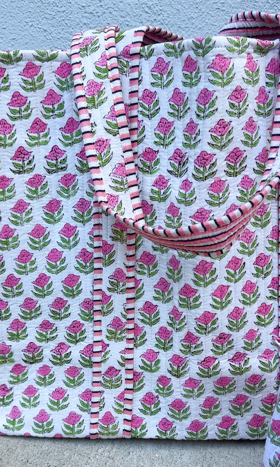 Floral patterned fabric with pink and green flowers on a white background, folded and displayed against a light blue wall.