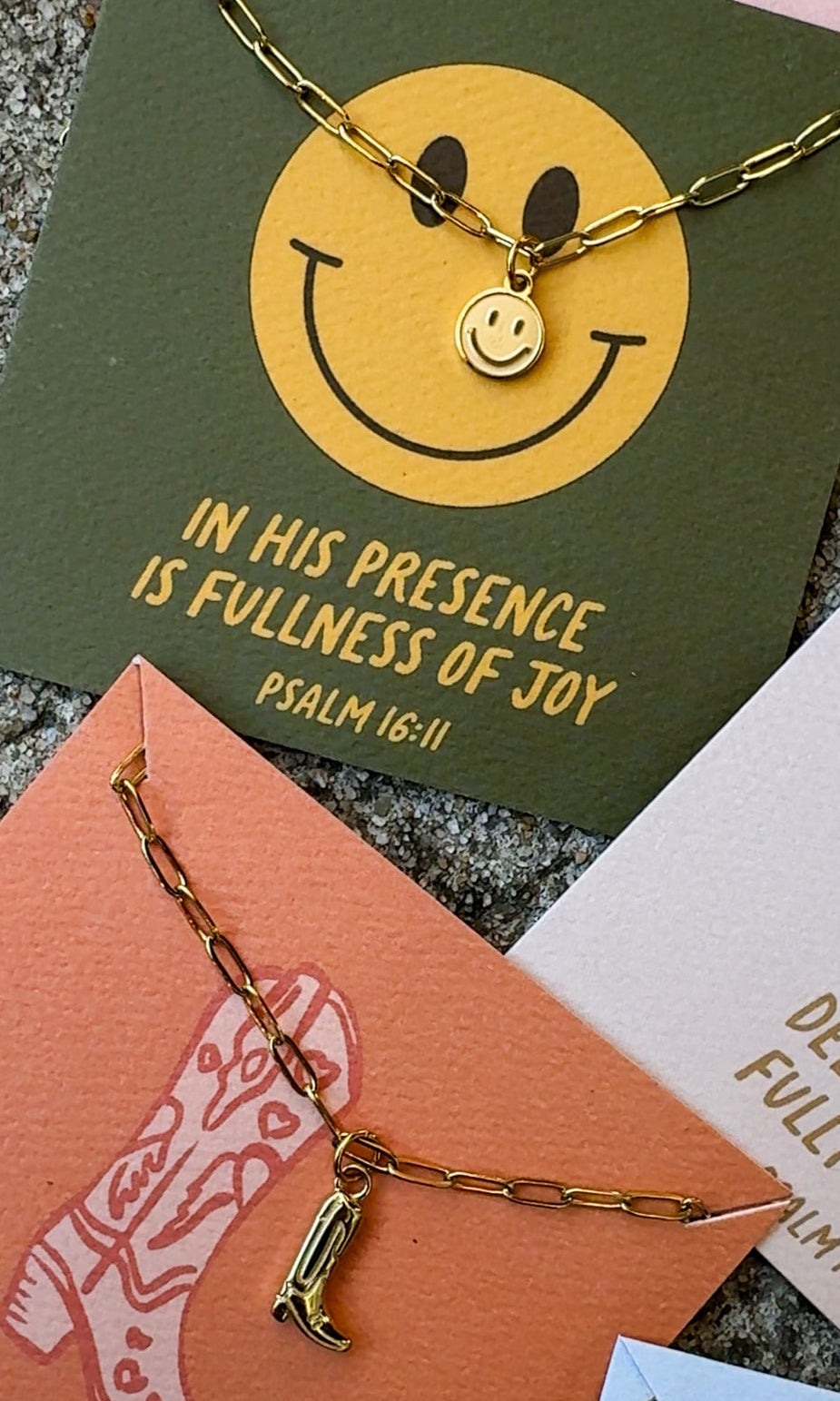 Gold necklace with a smiley face pendant on a textured surface with motivational cards.