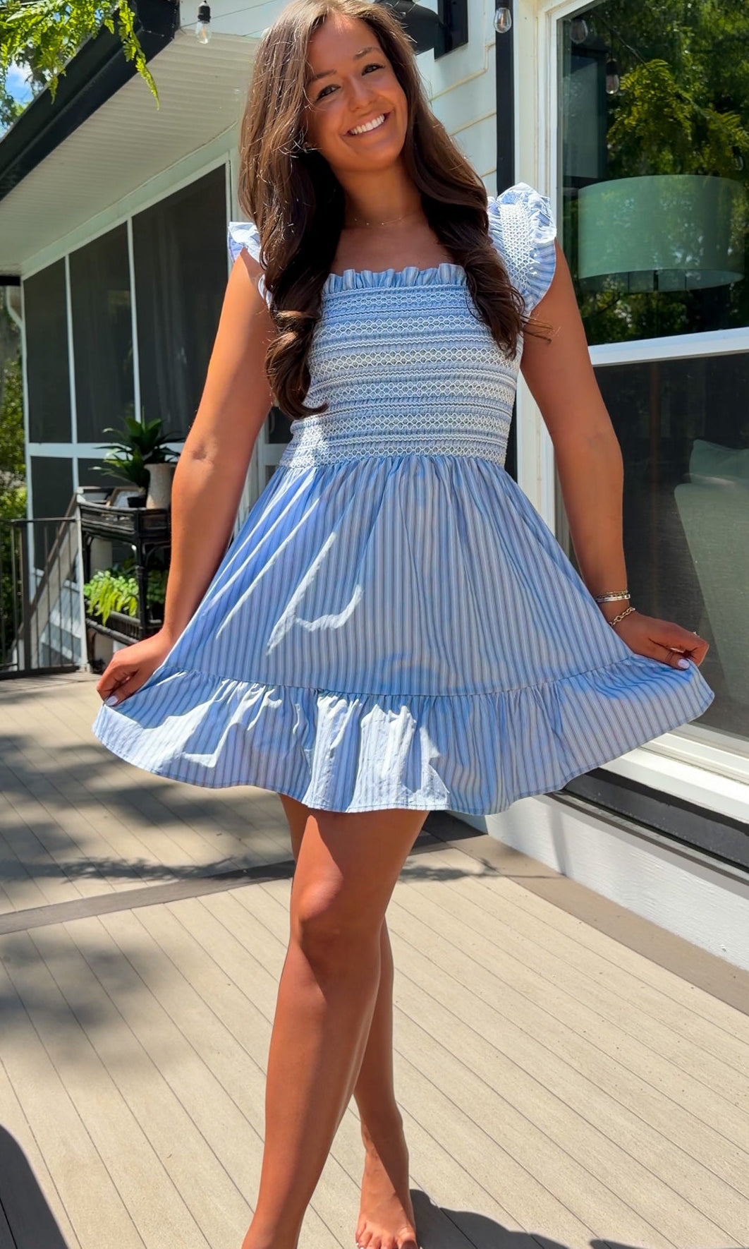Woman in a blue and white striped dress standing on a wooden deck.