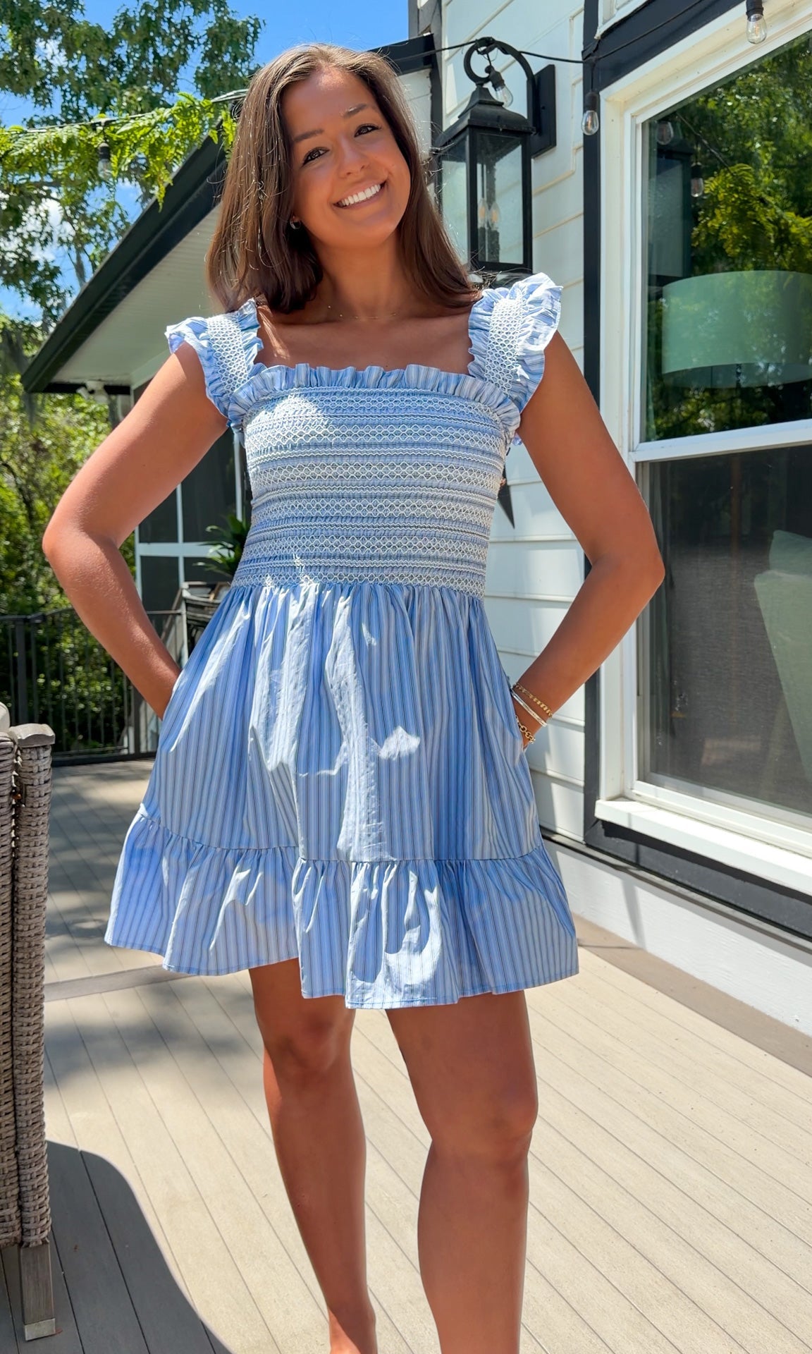 Woman wearing a blue and white dress standing on a deck with a house in the background