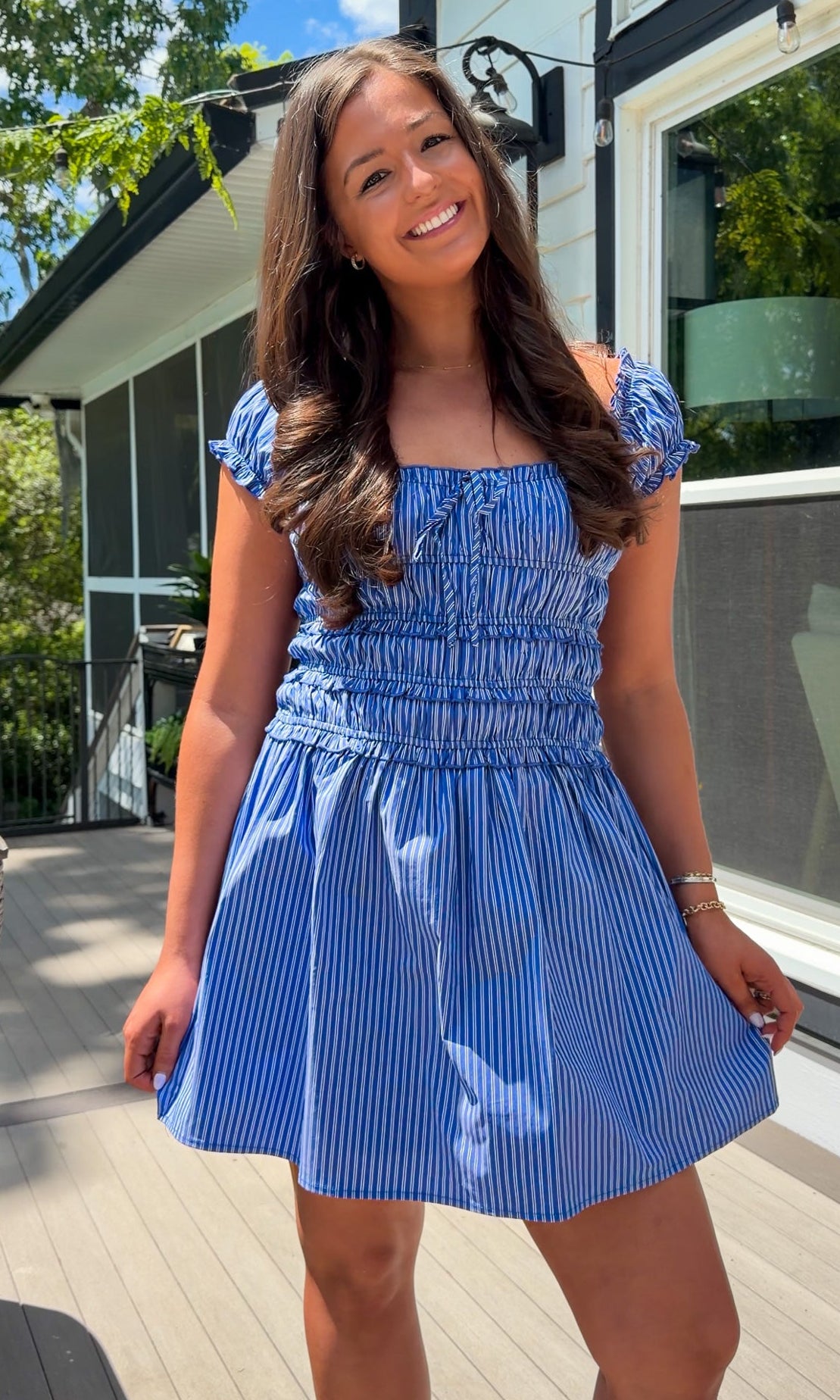 Woman wearing a blue dress standing outdoors on a wooden deck.