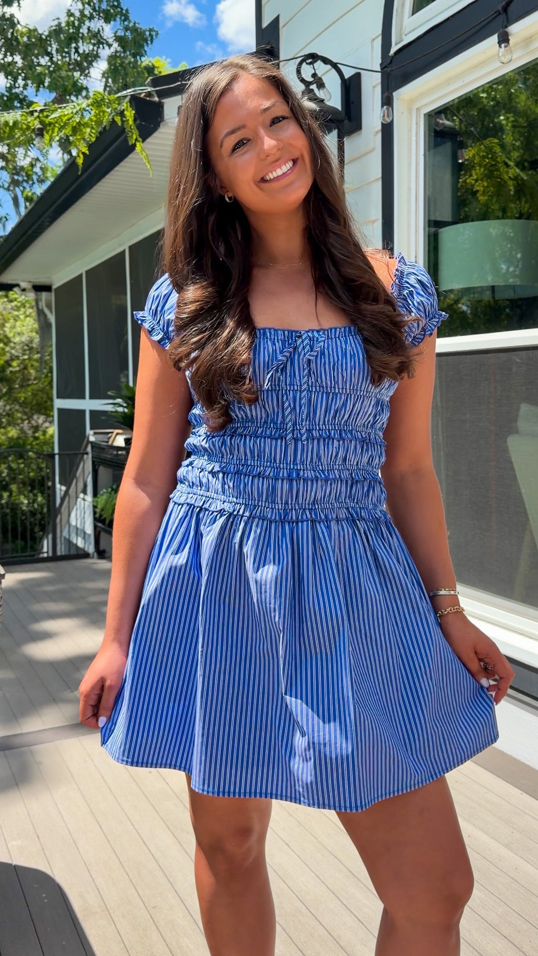 Woman wearing a blue dress standing outdoors on a wooden deck.