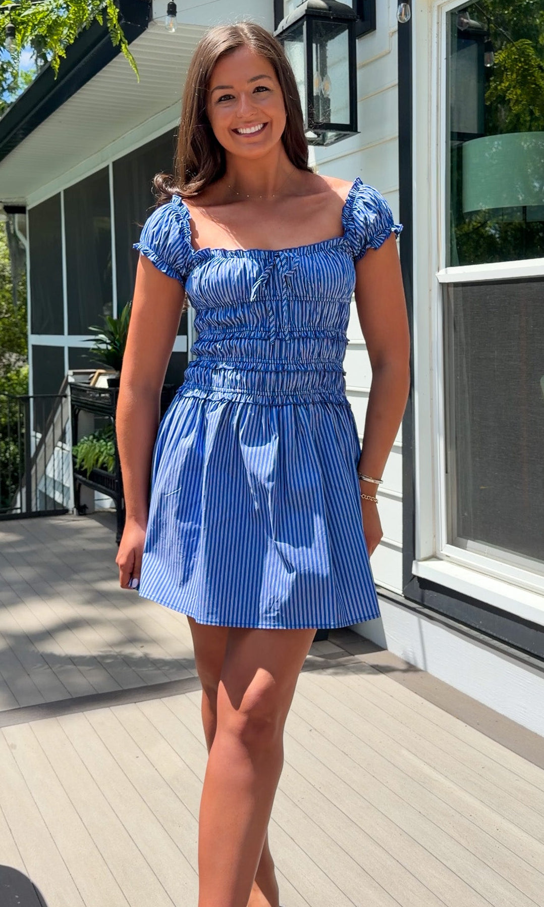 Woman in a blue dress standing on a wooden deck with a house in the background