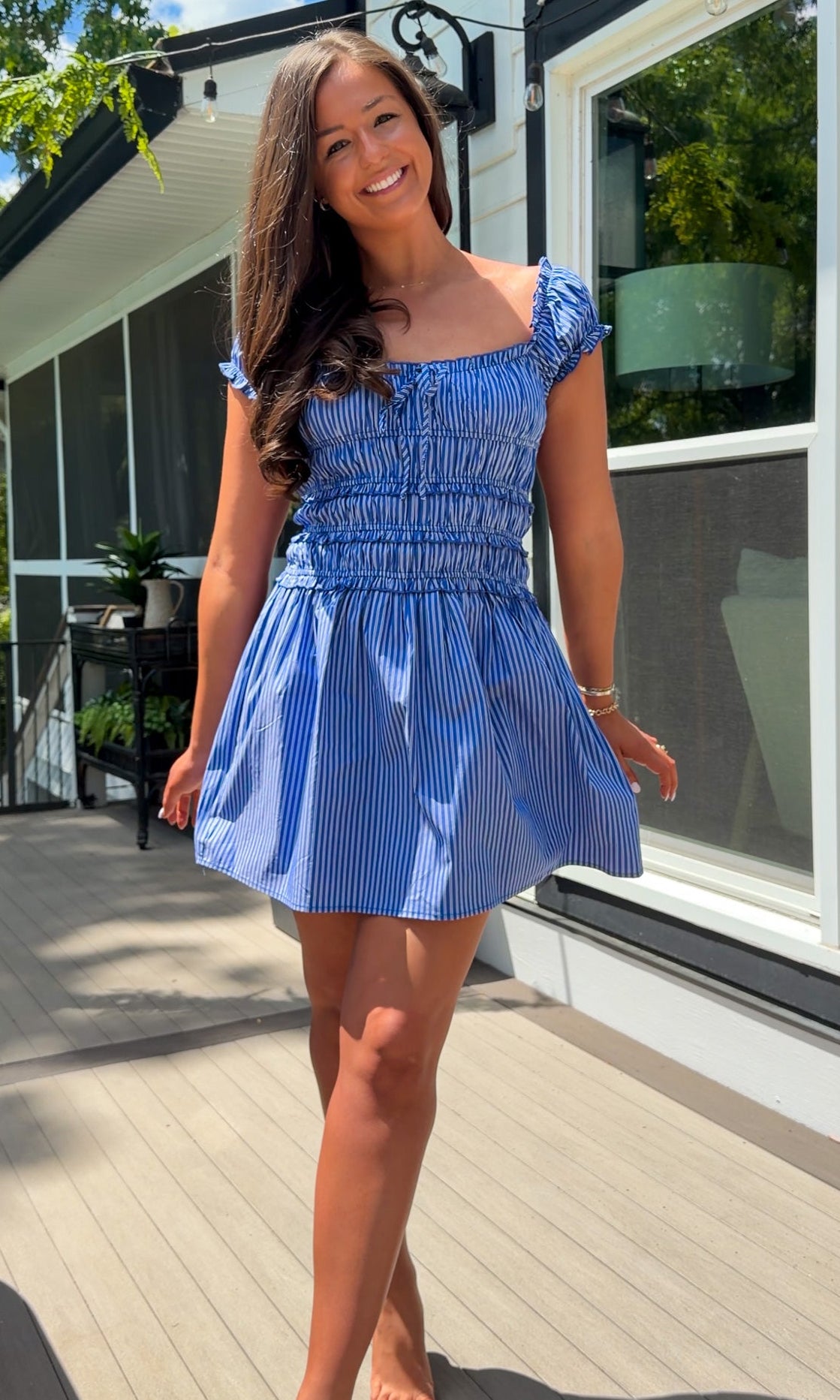 Woman in a blue dress standing on a wooden deck with a house in the background