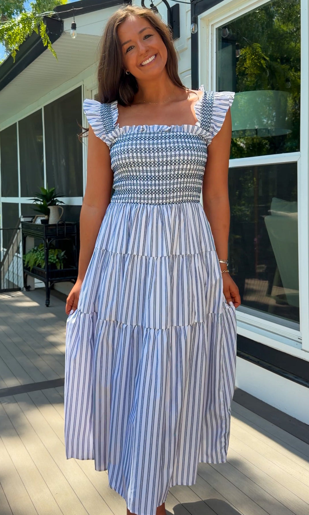Woman wearing a blue and white striped dress standing on a wooden deck.