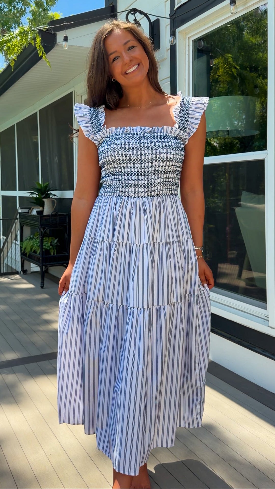 Woman wearing a blue and white striped dress standing on a wooden deck.