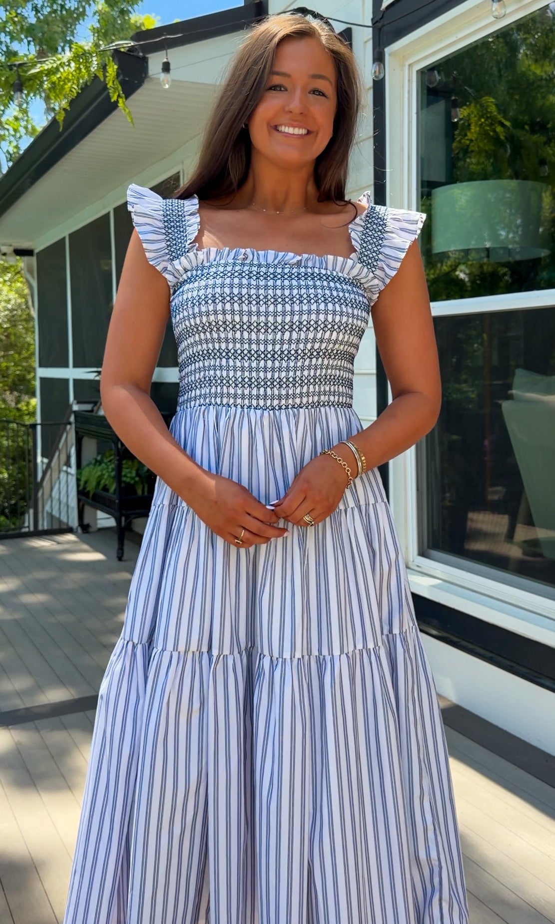 Woman in a blue and white striped dress standing outdoors near a house.