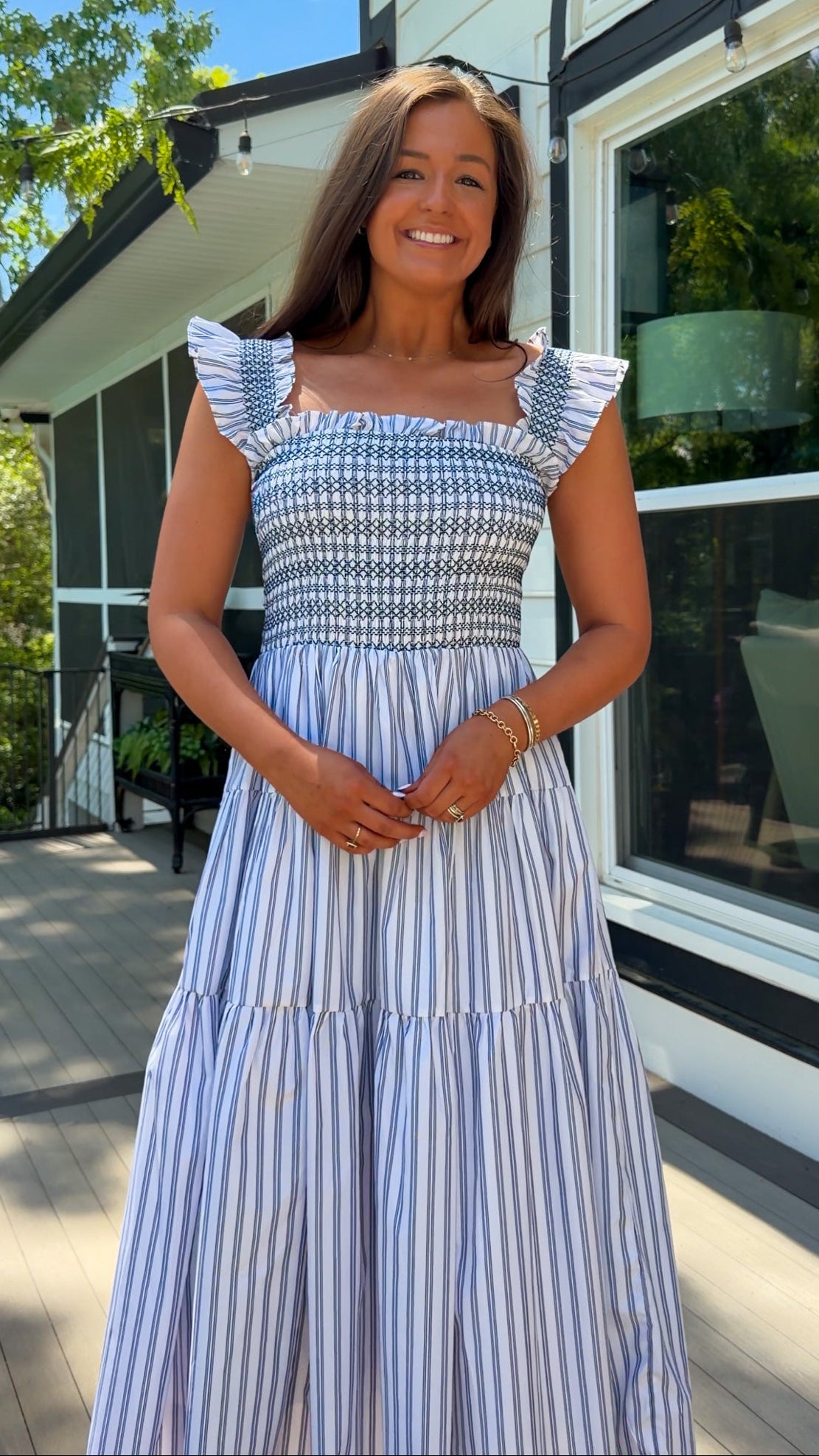 Woman in a blue and white striped dress standing outdoors near a house.