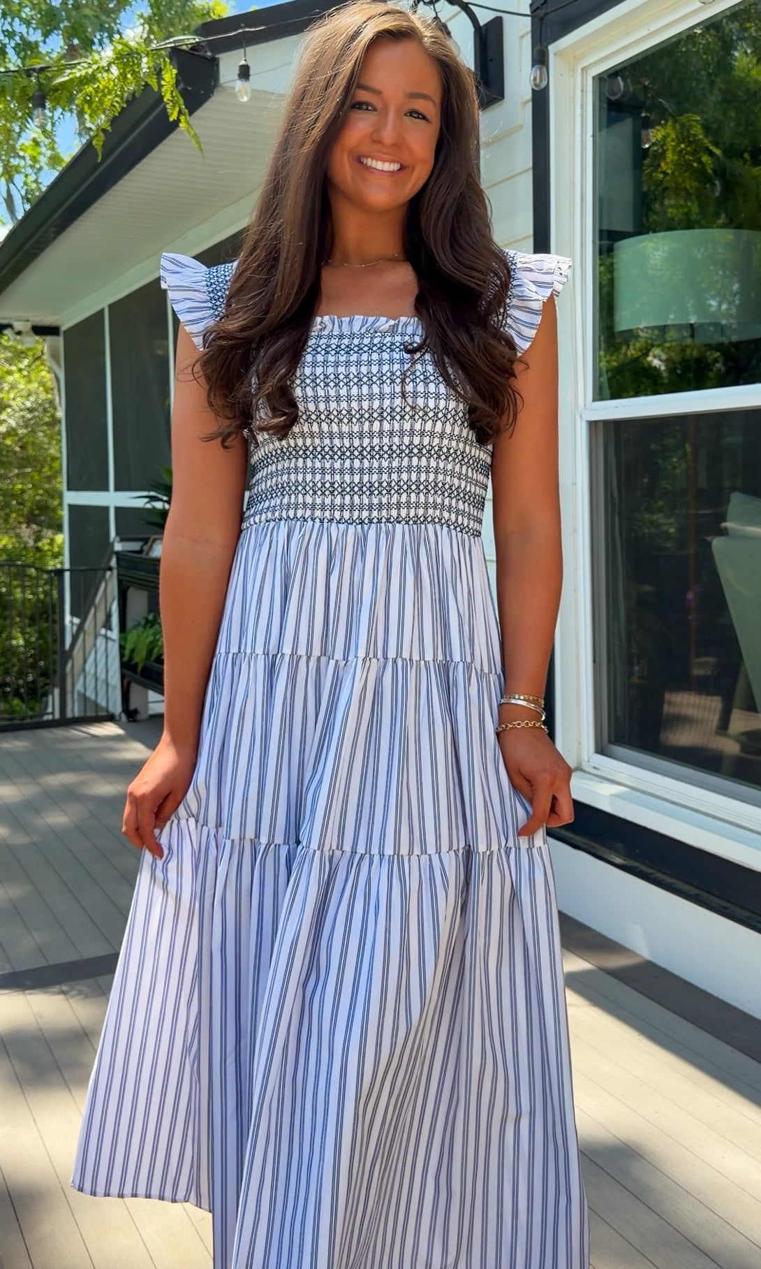 Woman wearing a blue and white striped dress standing outside a house.