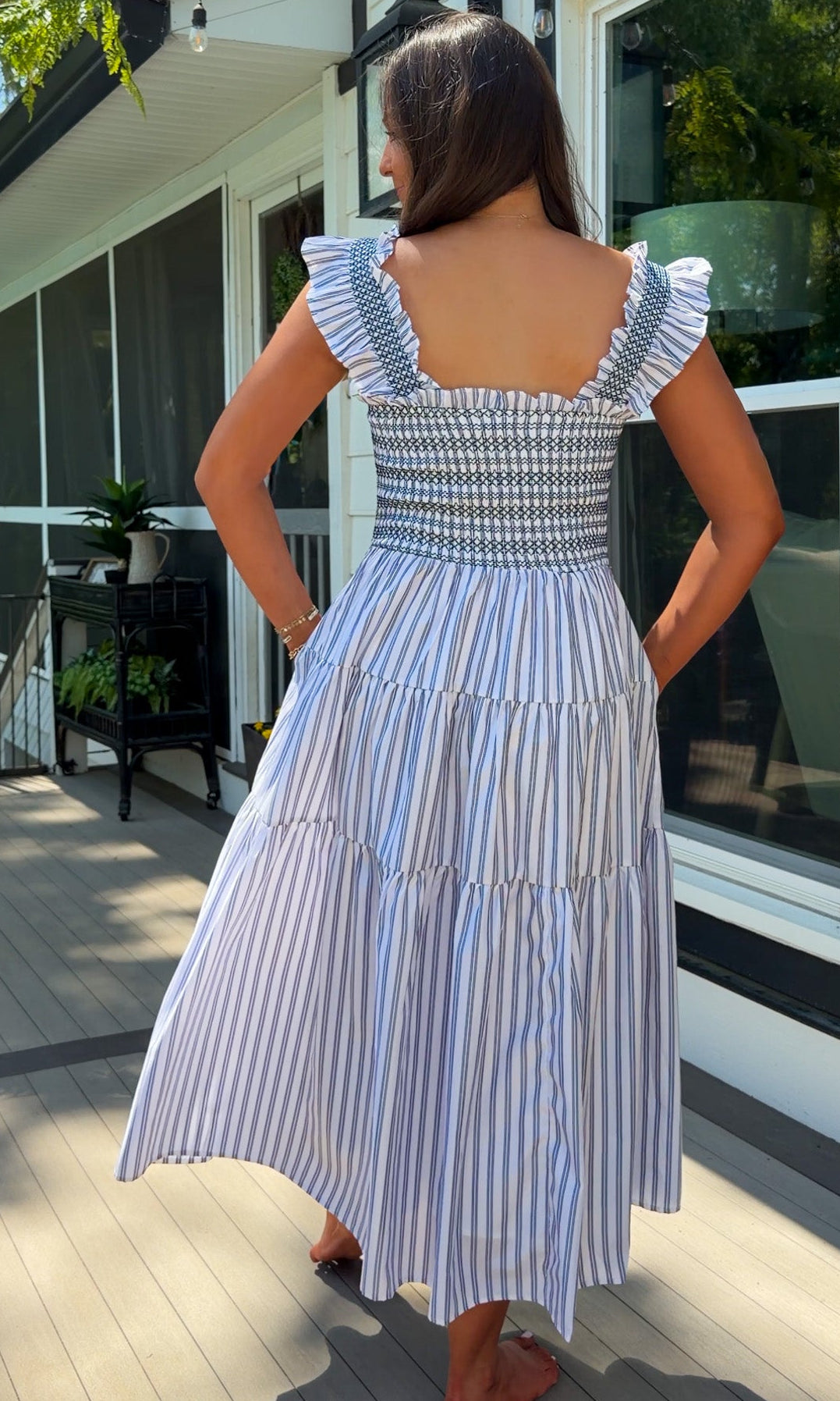 Woman in a blue and white striped dress standing on a wooden deck.