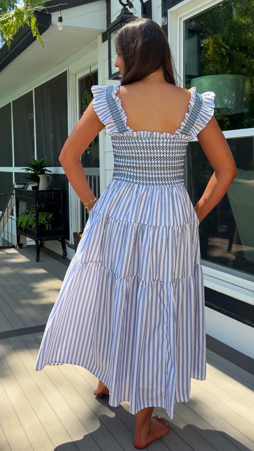 Woman in a blue and white striped dress standing on a wooden deck.
