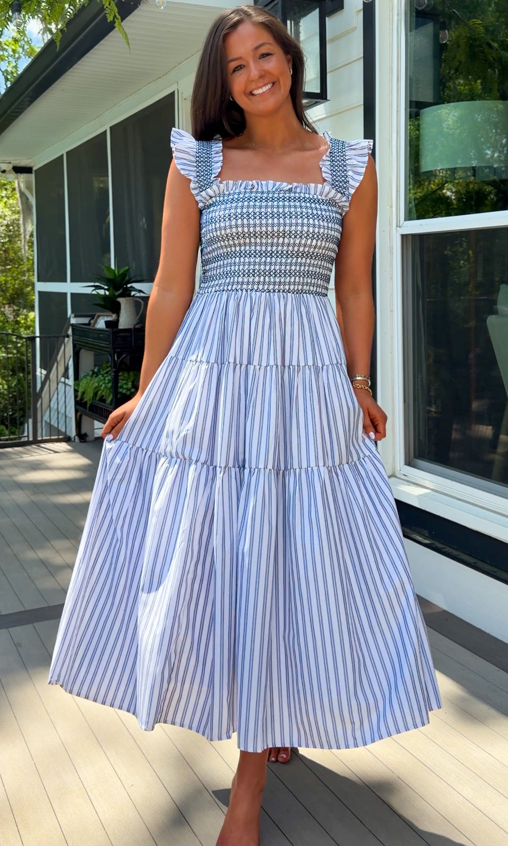 Woman wearing a blue and white striped dress standing on a porch.