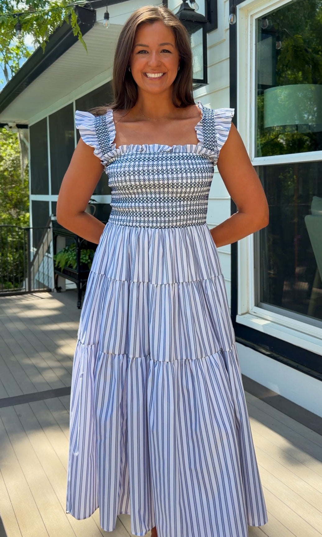 Woman wearing a blue and white checkered top and striped skirt standing on a porch.