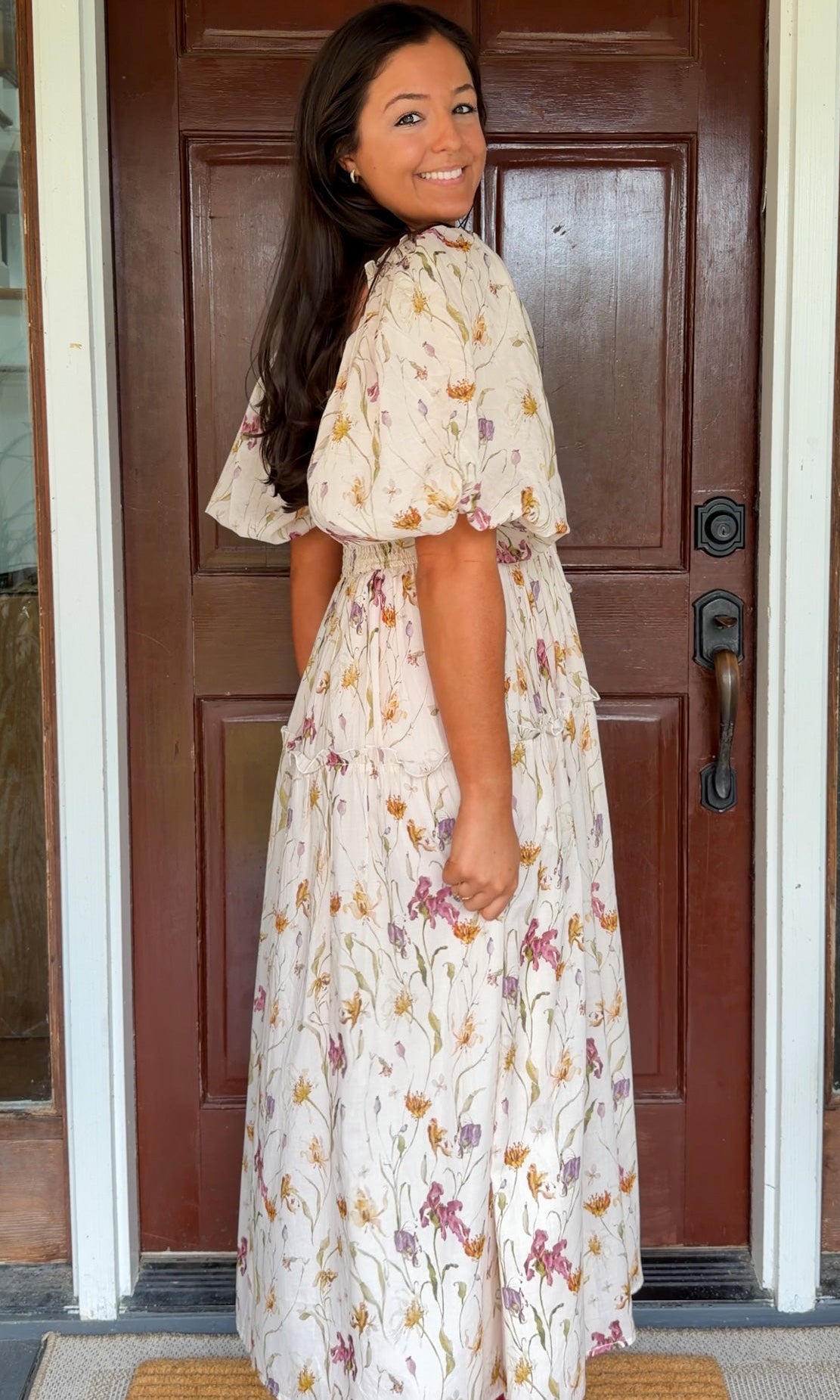 Model wearing a cream floral smocked midi dress with puff sleeves, flowy skirt, and side pockets,