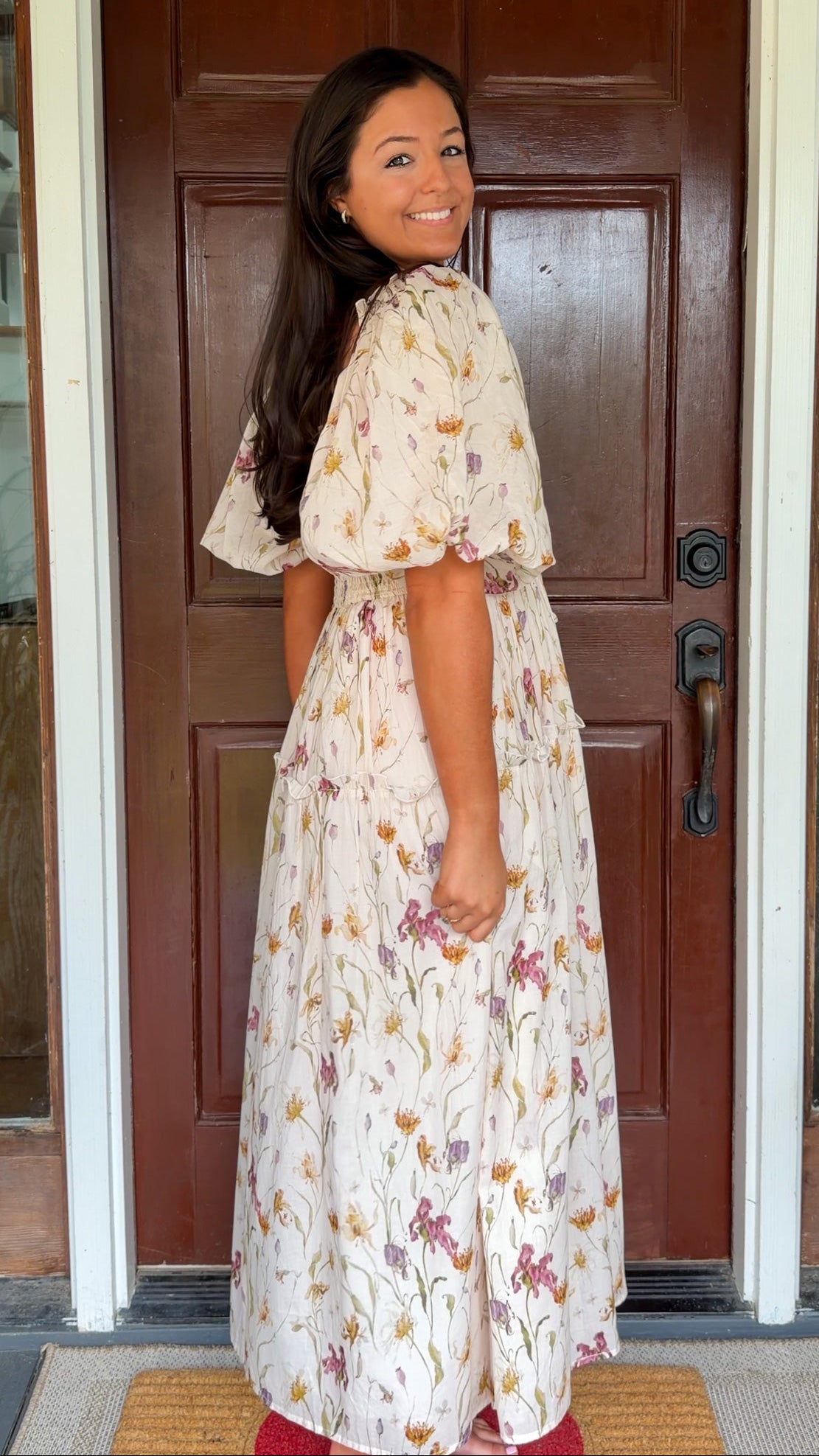 Model wearing a cream floral smocked midi dress with puff sleeves, flowy skirt, and side pockets,