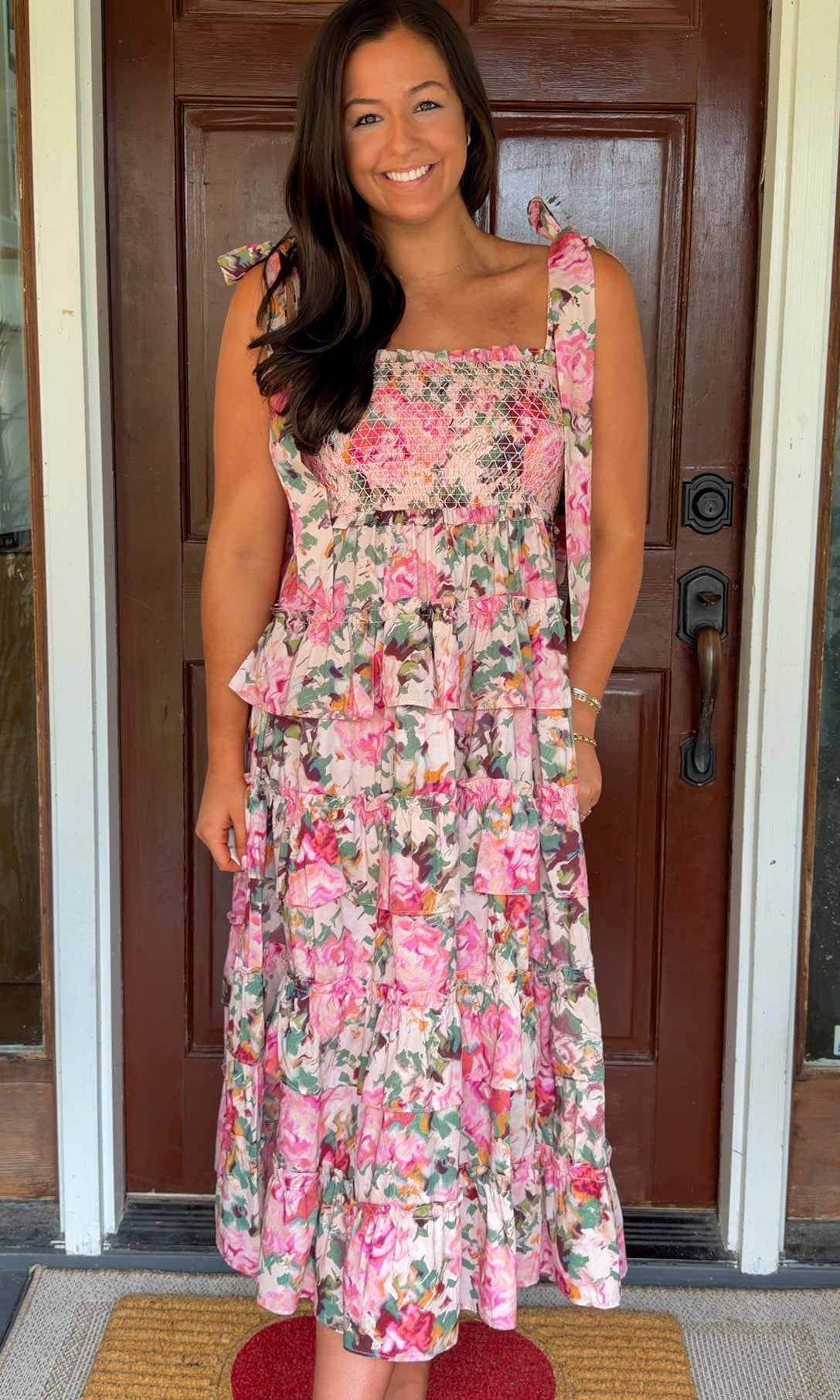 Woman wearing a floral dress standing in front of a wooden door.