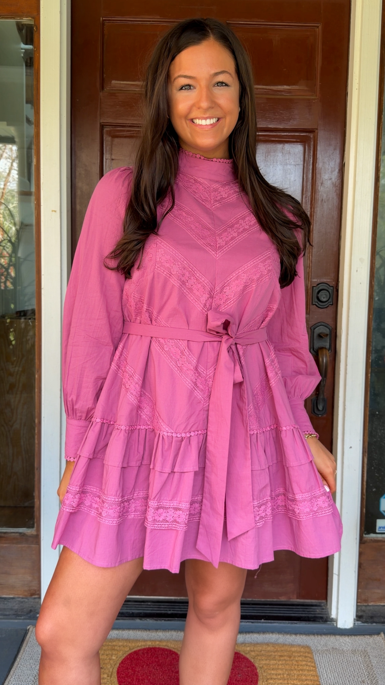 Woman wearing a pink dress standing in front of a door.