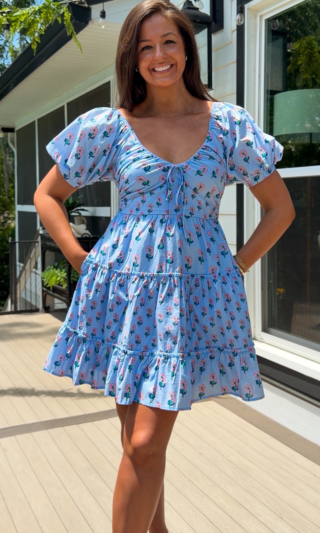 Woman wearing a blue dress with a floral pattern standing outdoors.
