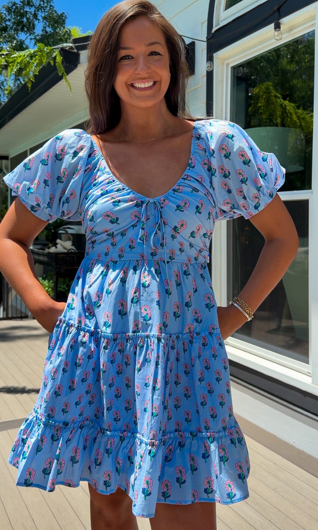 Woman wearing a blue dress with floral pattern standing outdoors.