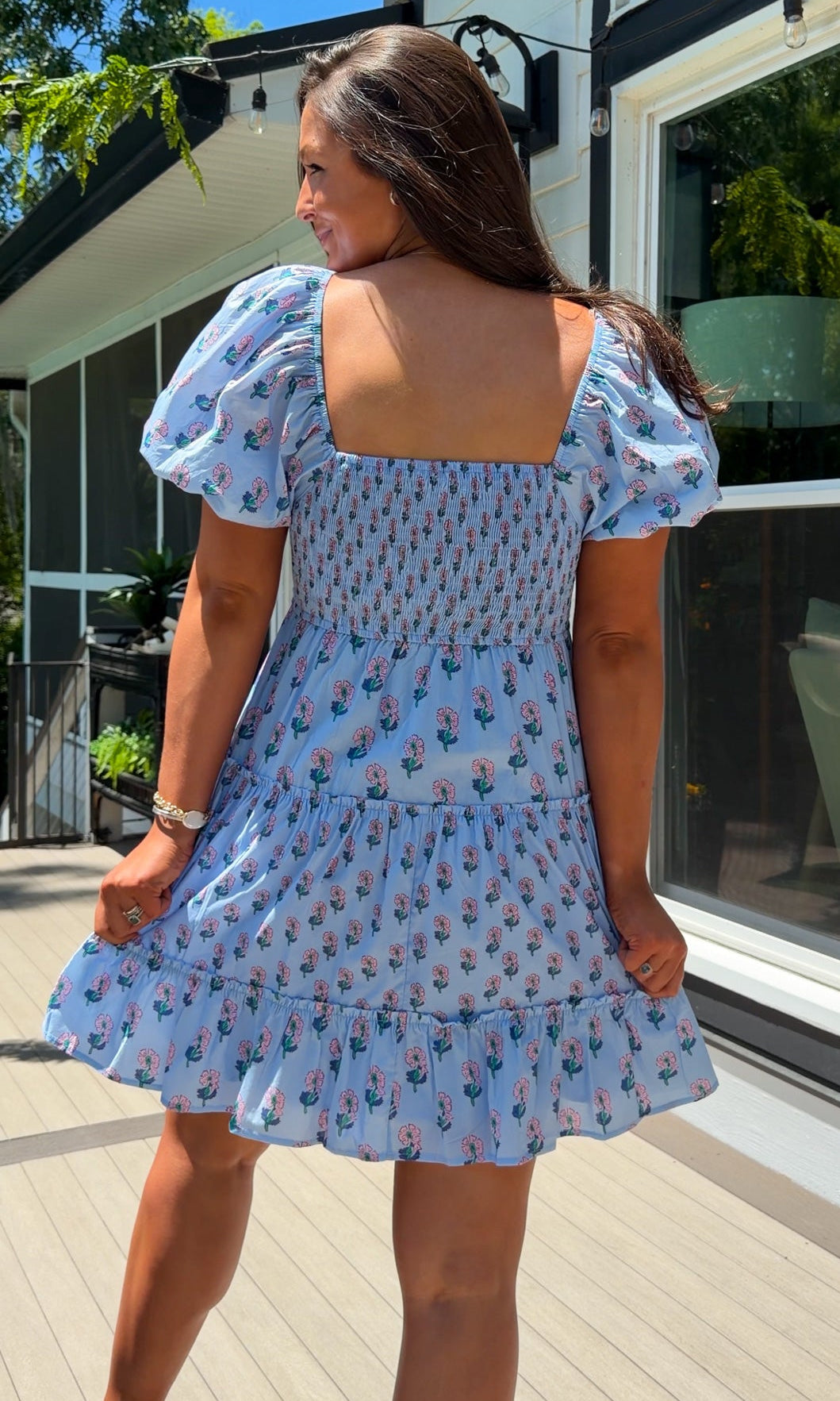 Woman wearing a blue floral dress standing on a wooden deck.